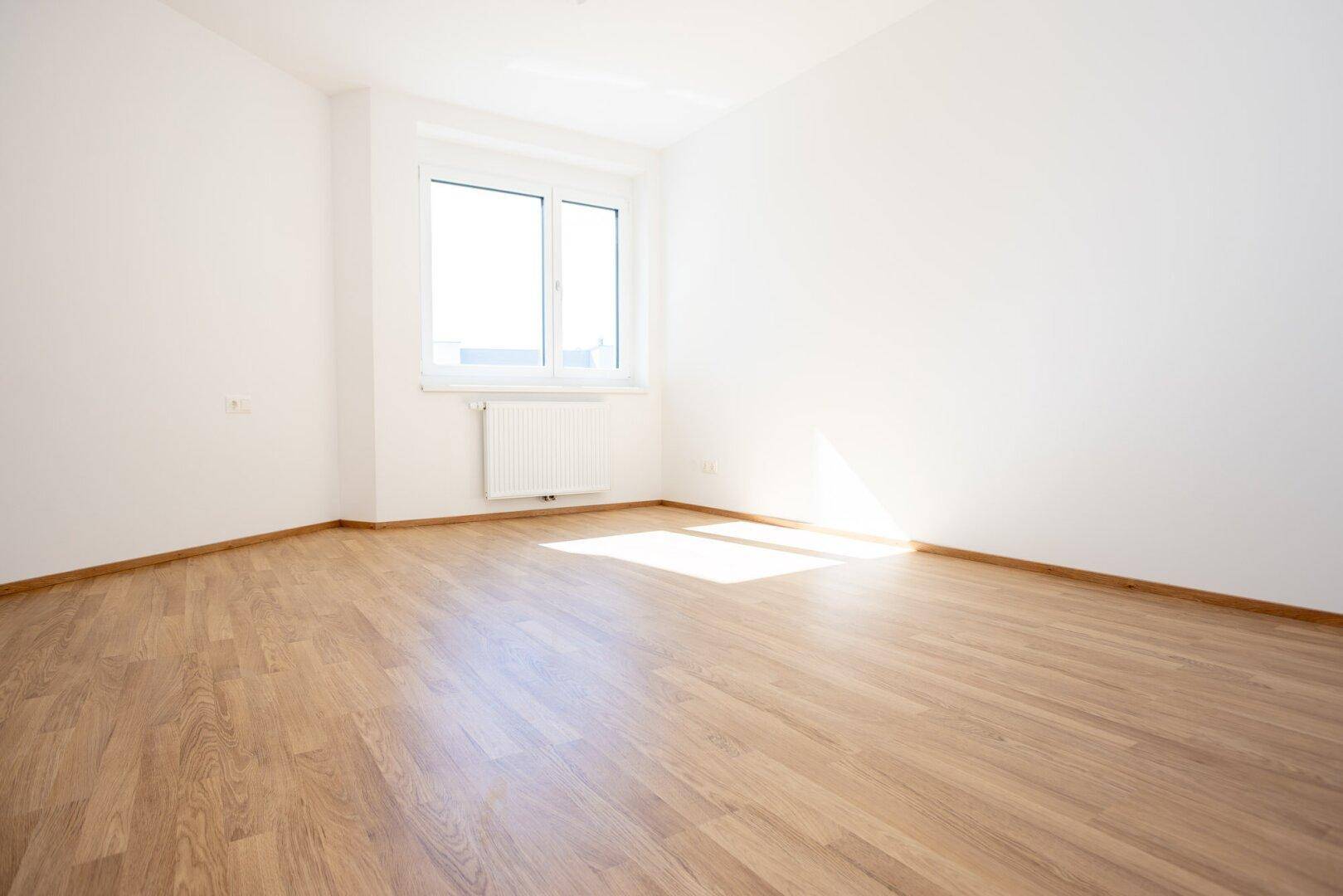 Helles Schlafzimmer mit Laminatboden und einem großen Fenster.