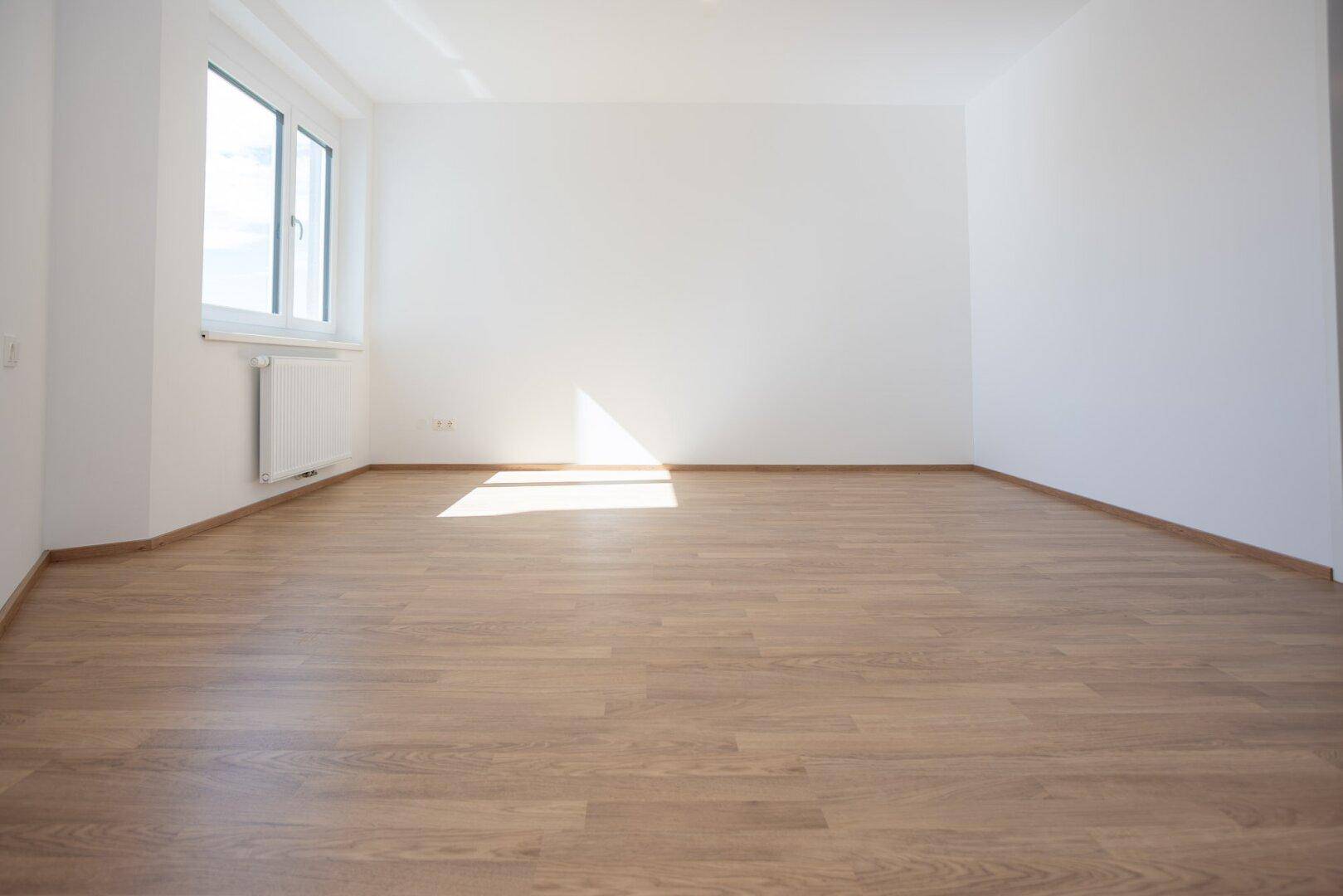 Geräumiges, helles Zimmer mit Laminatboden und viel Tageslicht.