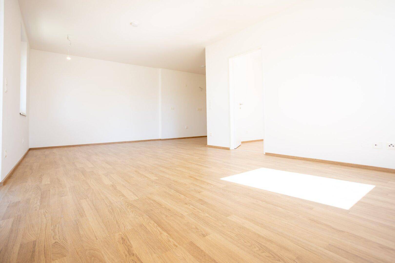 Großes, helles Zimmer mit Laminatboden und weiß gestrichenen Wänden.