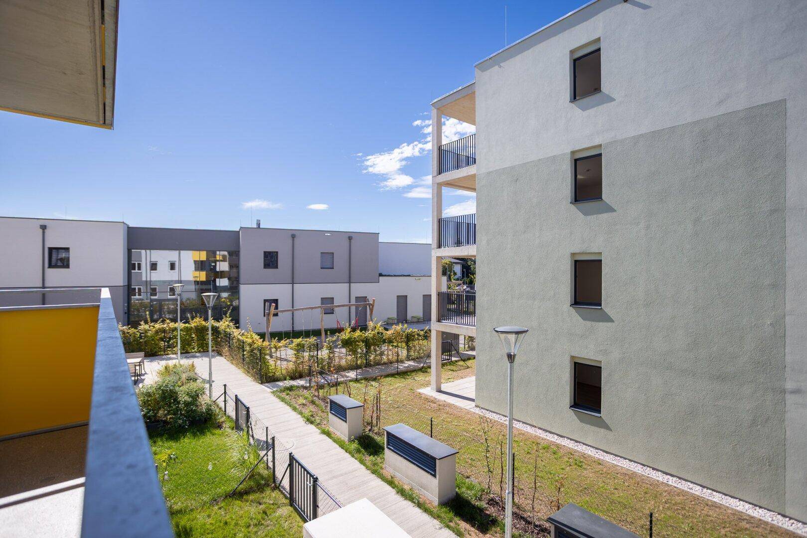 Blick vom Balkon auf den begrünten Innenhof einer modernen Wohnanlage.