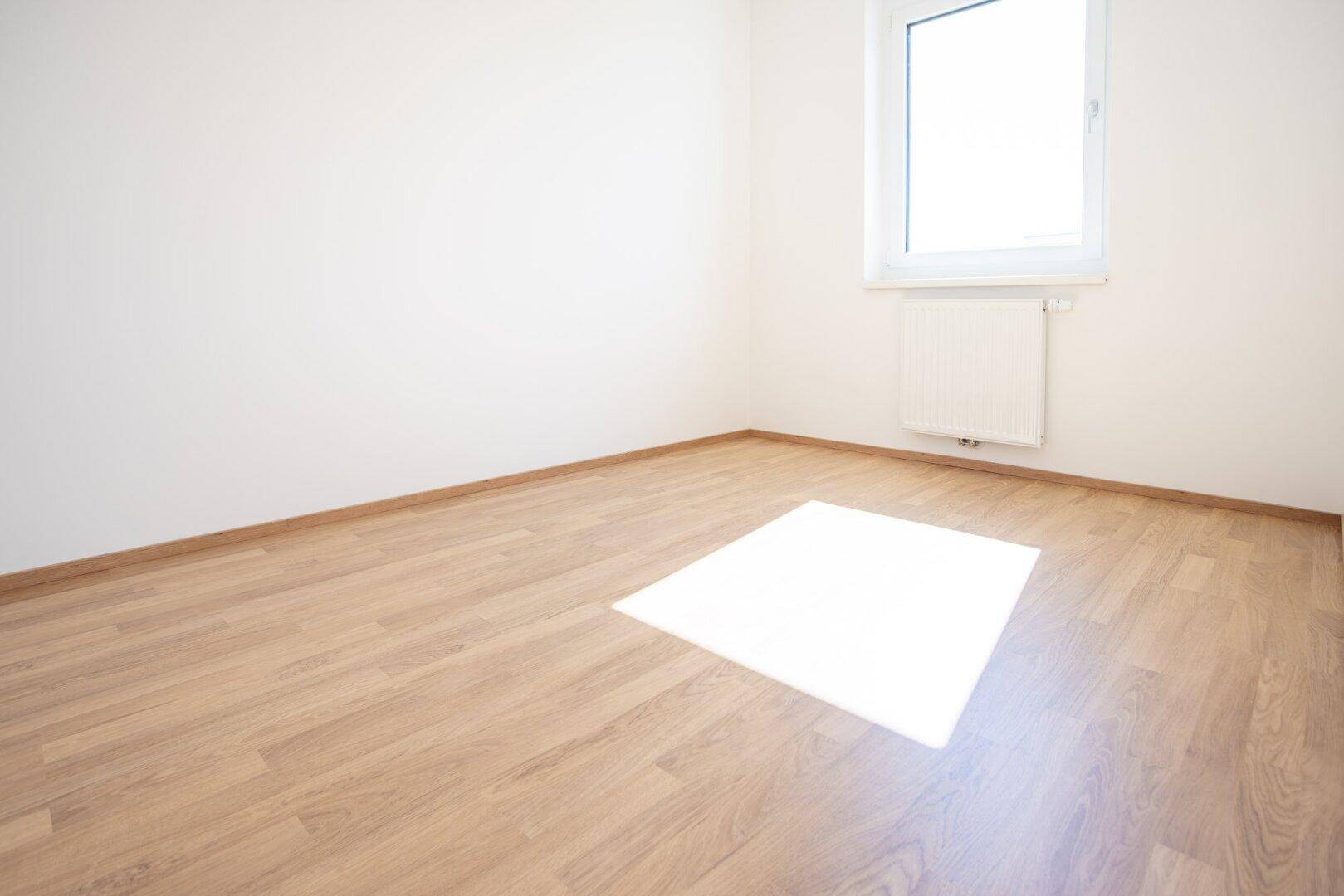 Helles Zimmer mit Laminatboden und einem Fenster, das den Raum erhellt.