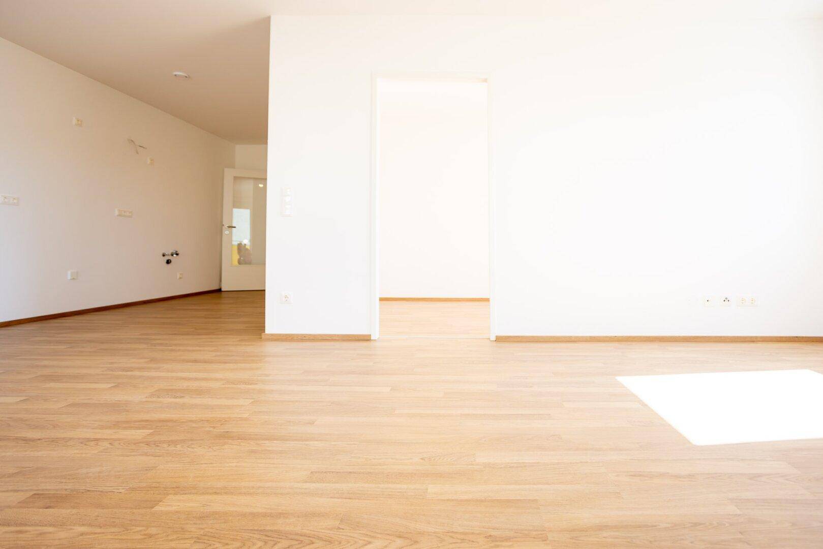 Heller Wohnbereich mit Laminatboden und offenen Durchgängen zu weiteren Räumen.