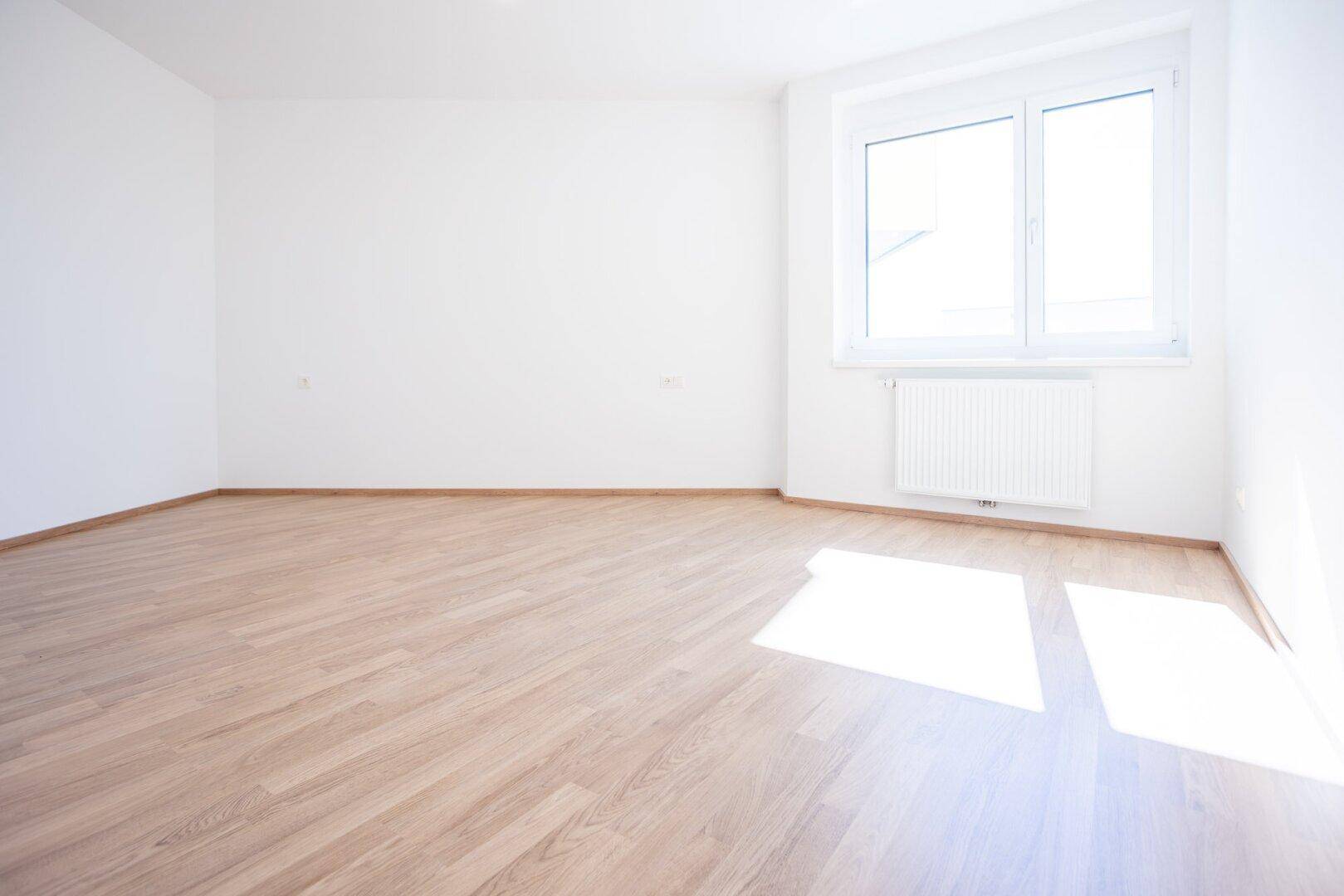 Sonniger Raum mit Laminatboden und einem Fenster, das viel Licht hereinlässt.