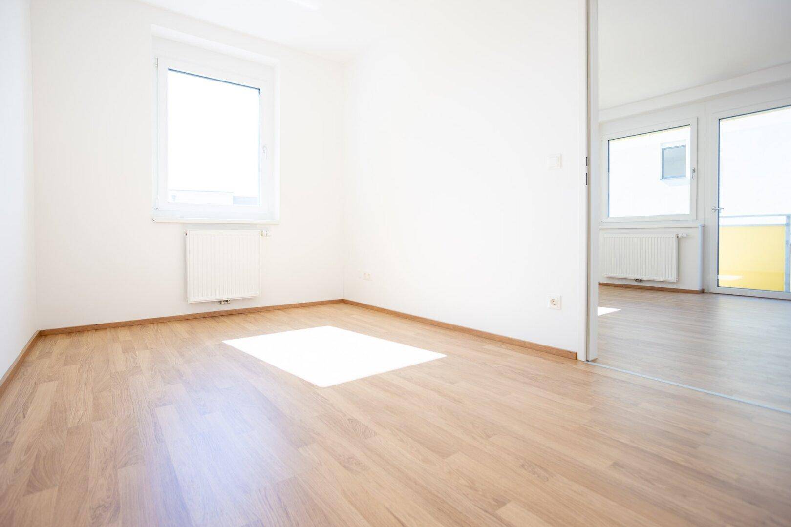 Helles Zimmer mit Laminatboden und einem Spiegel, der den angrenzenden Raum reflektiert.