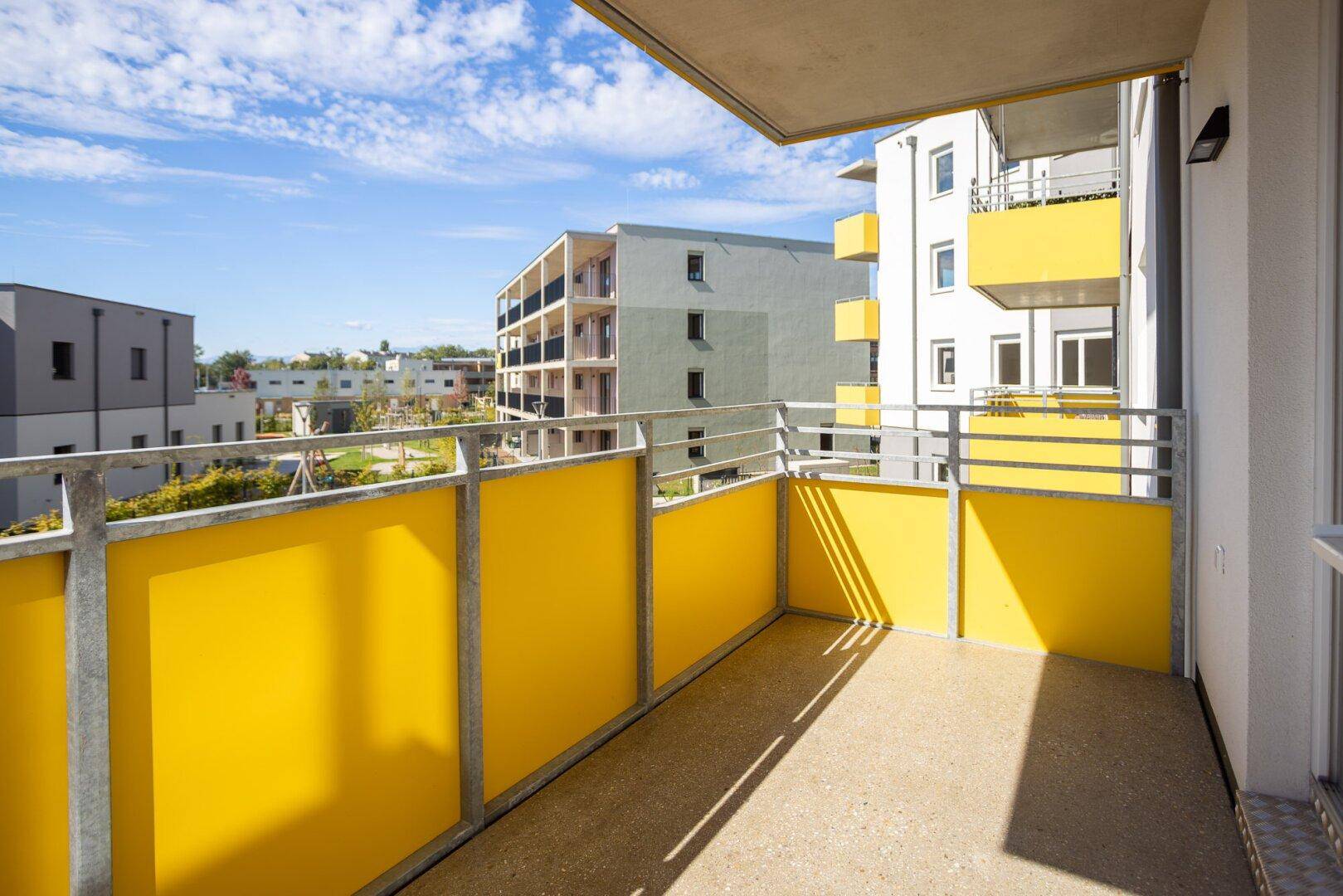 Heller Balkon mit gelben Sichtschutzelementen und Blick auf moderne Wohngebäude.