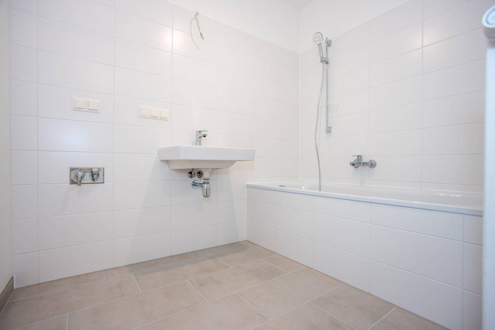 Modernes Badezimmer mit weißen Wandfliesen, grauen Bodenfliesen, Waschbecken und Badewanne.