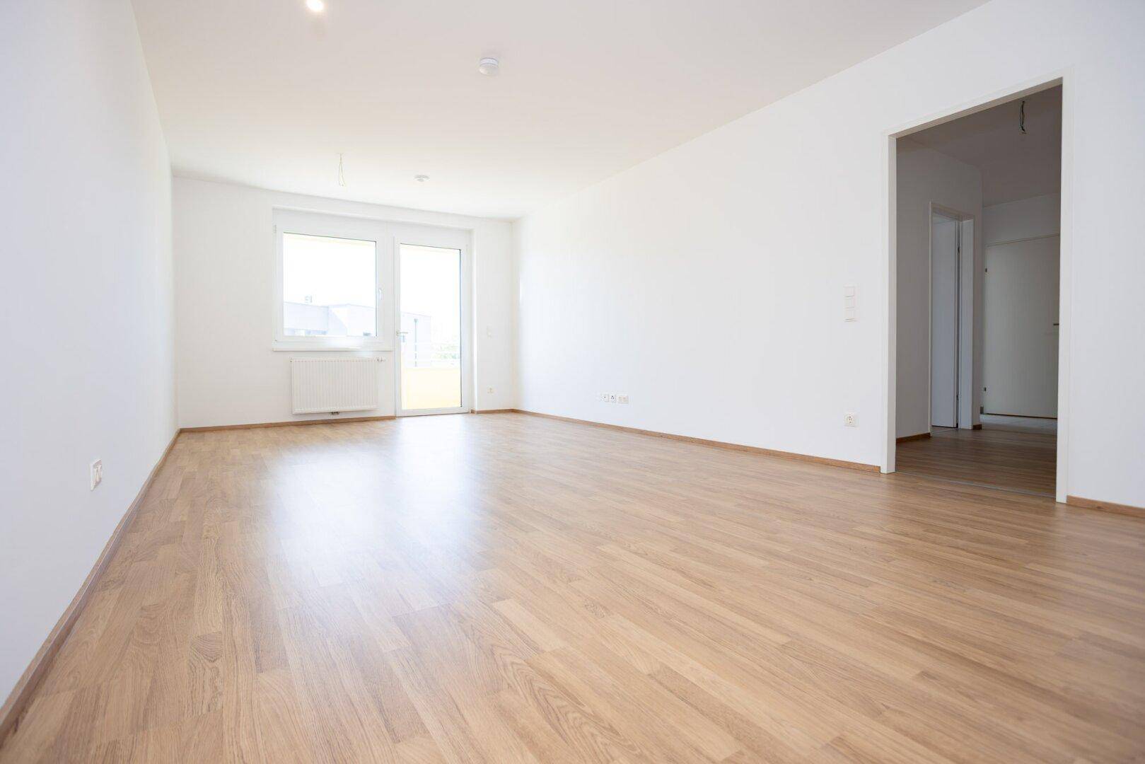 Geräumiges, helles Zimmer mit Laminatboden und Zugang zu einem weiteren Raum sowie einem Balkon.