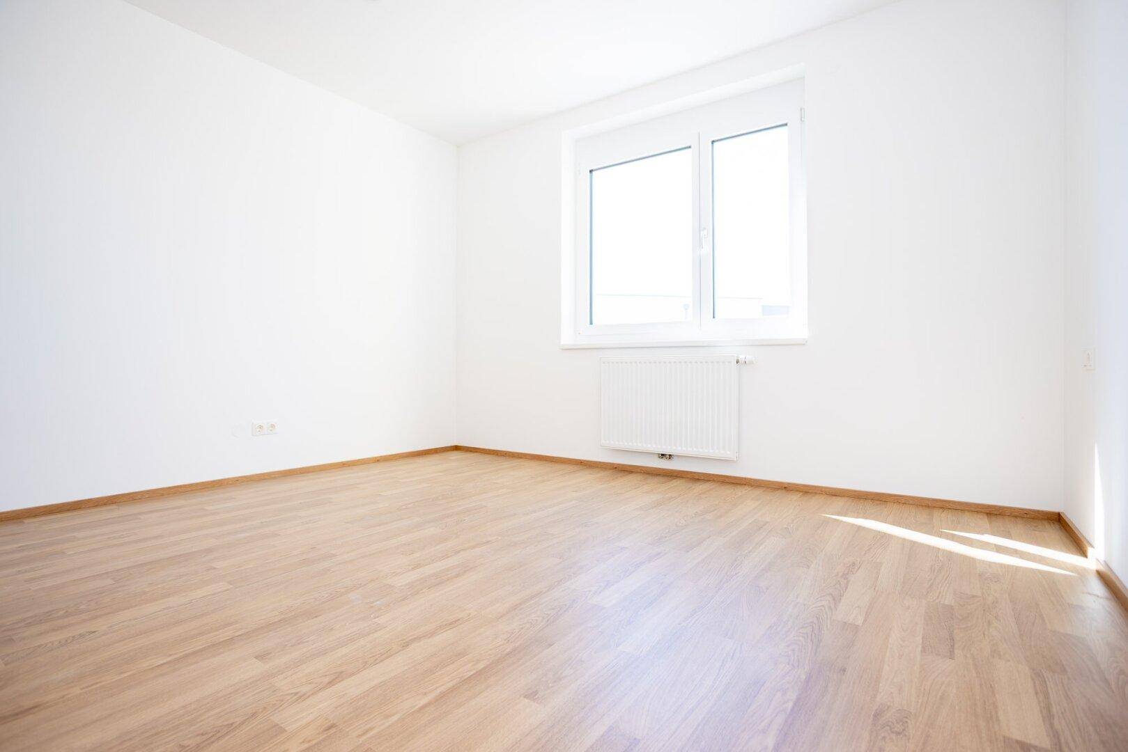 Geräumiges, helles Schlafzimmer mit Laminatboden und einem großen Fenster für viel Tageslicht.