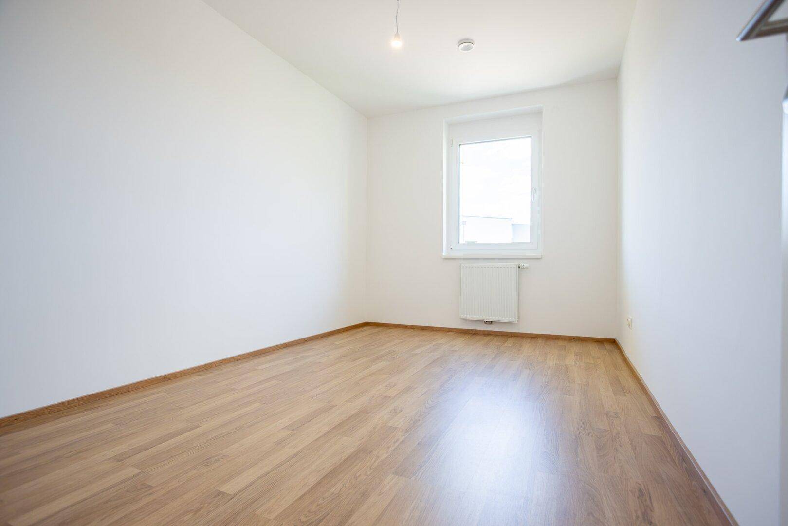 Ruhiges Schlafzimmer mit Laminatboden und weißen Wänden, ideal für erholsame Nächte.