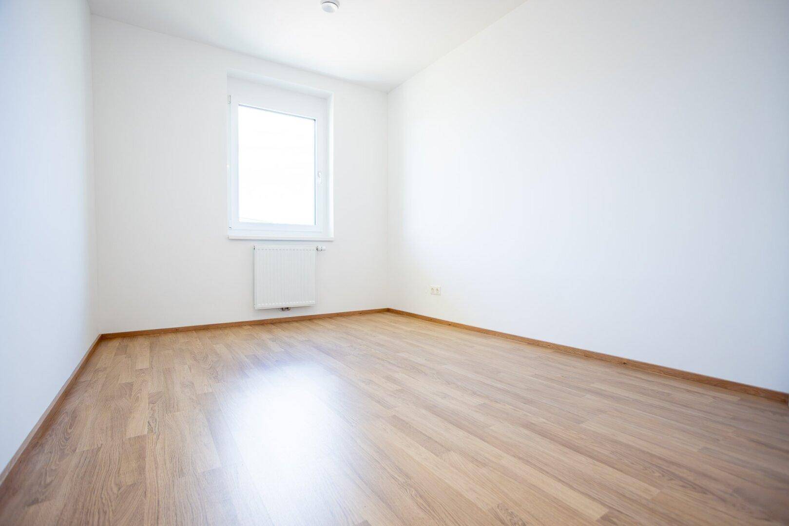 Freundliches Schlafzimmer mit Laminatboden und einem Fenster, das viel Tageslicht hereinlässt.