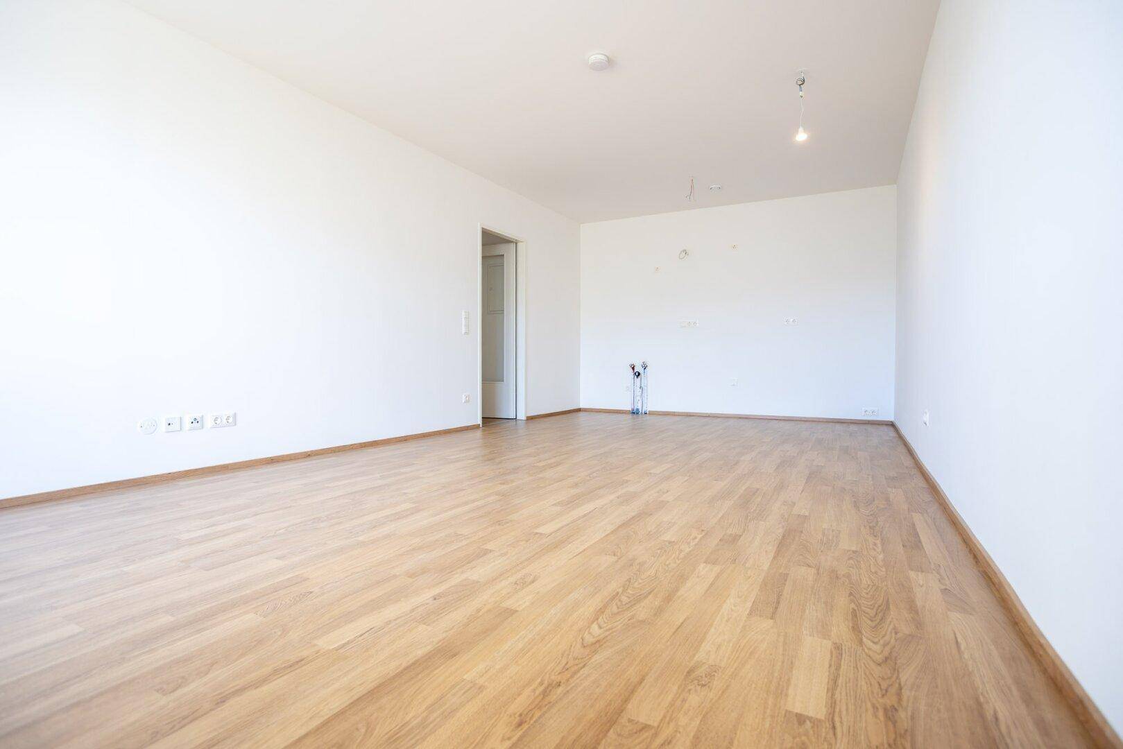 Leeres, helles Zimmer mit Laminatboden und weißen Wänden, bereit zur individuellen Gestaltung.