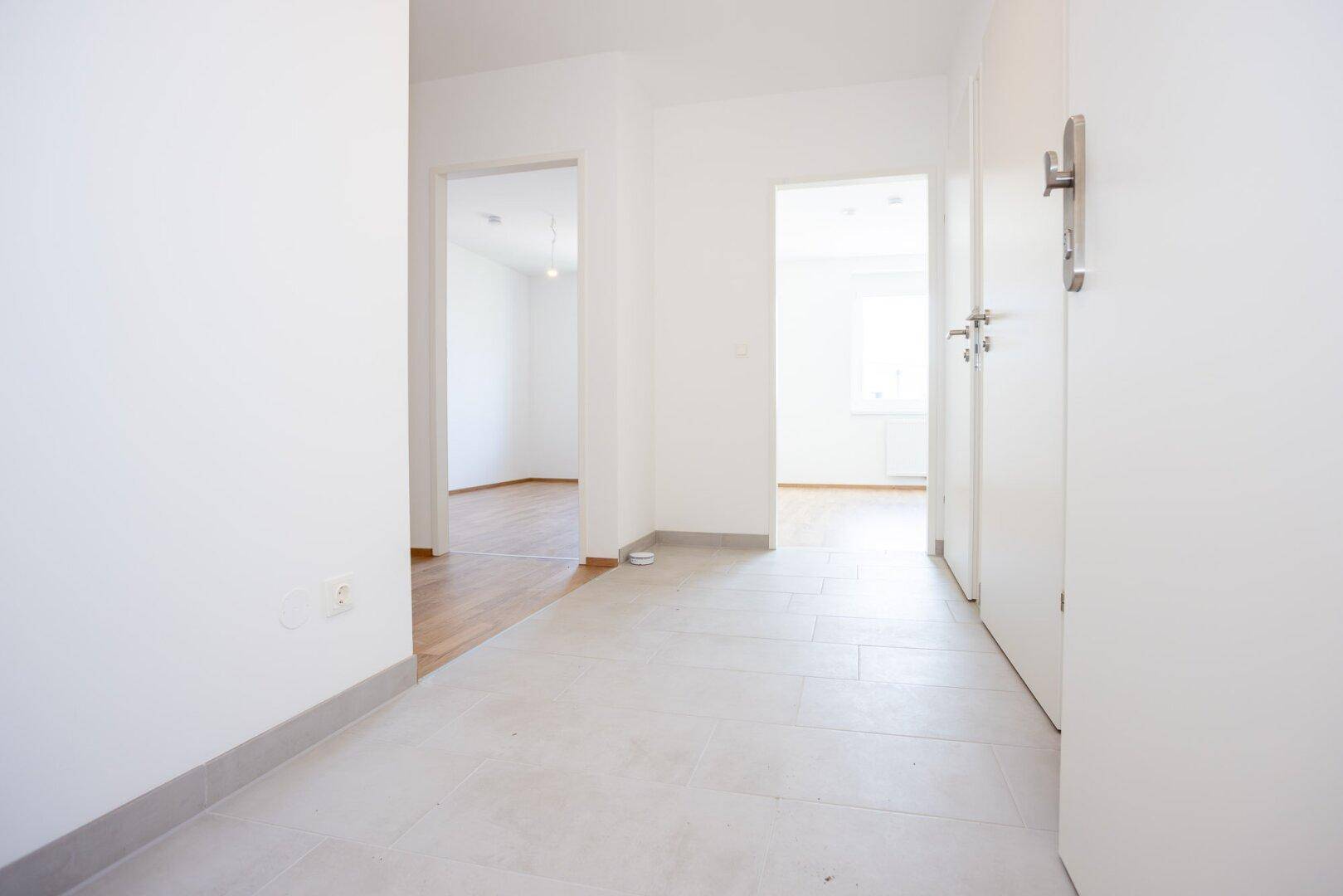 Heller Flur mit grauen Bodenfliesen und Zugang zu verschiedenen Zimmern der Wohnung.