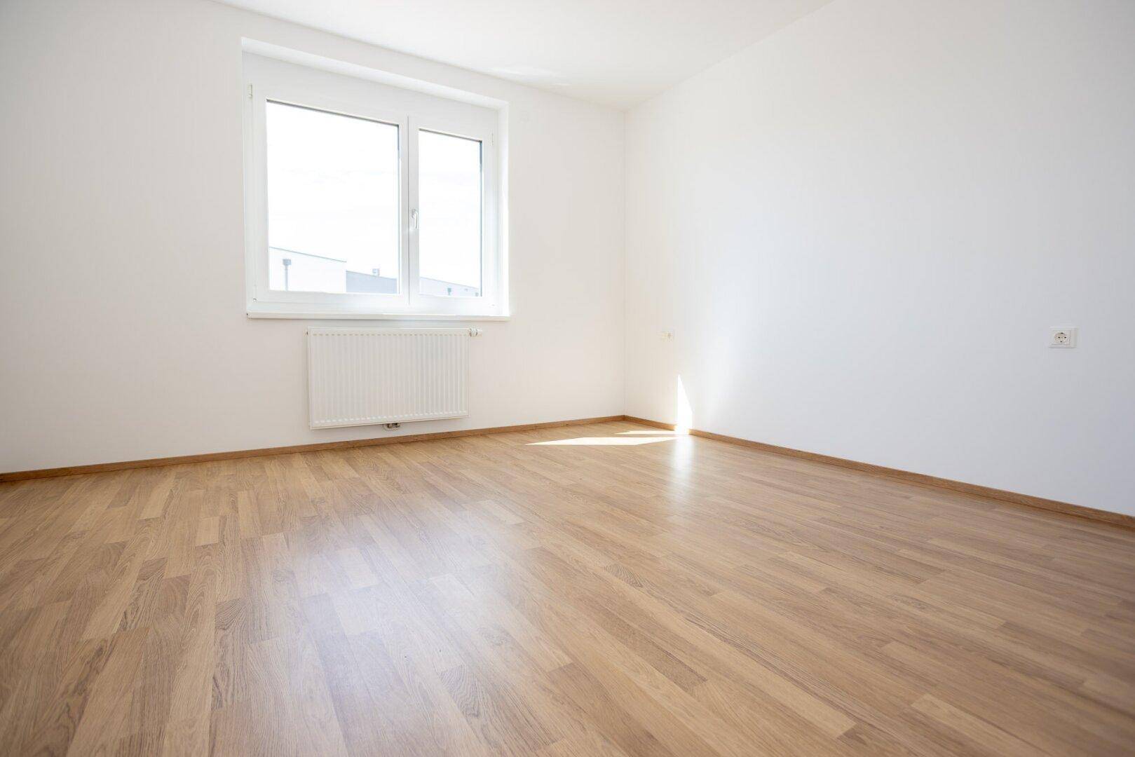 Helles Schlafzimmer mit Laminatboden und einem Fenster, das viel Tageslicht hereinlässt.