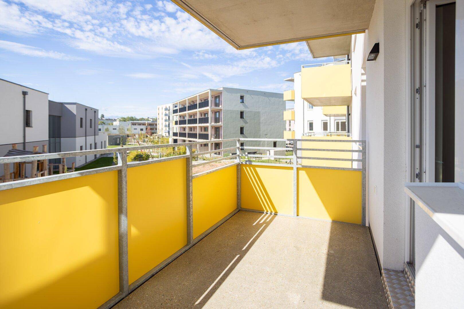 Heller Balkon mit gelben Sichtschutzelementen und Blick auf die umliegende Wohnsiedlung.