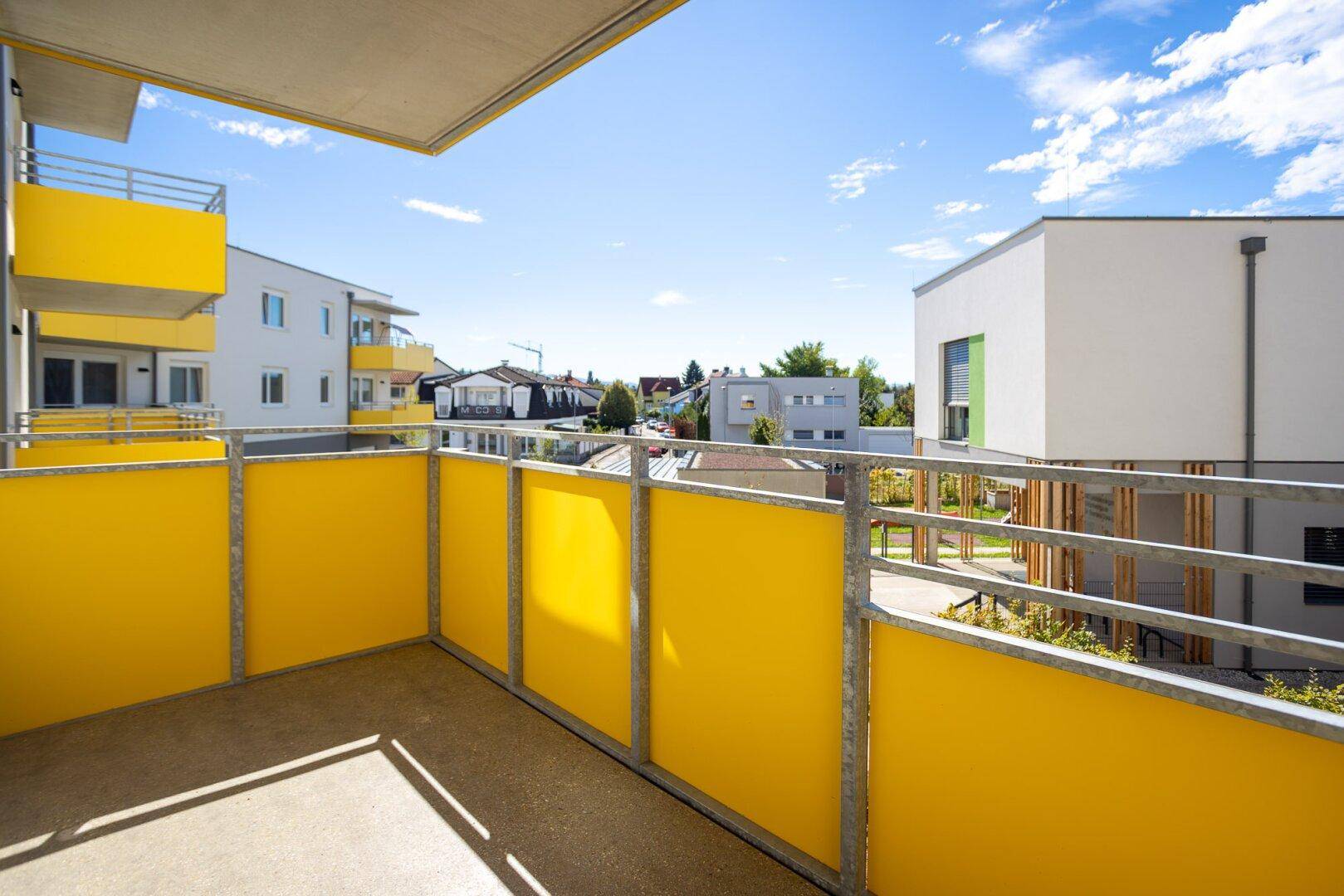 Sonniger Balkon mit gelben Brüstungselementen und weitem Blick über die Nachbarschaft.
