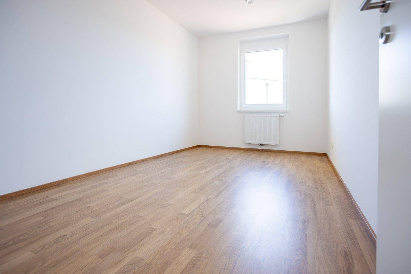 Freundliches Zimmer mit Laminatboden und einem Fenster, ideal als Schlaf- oder Arbeitszimmer.