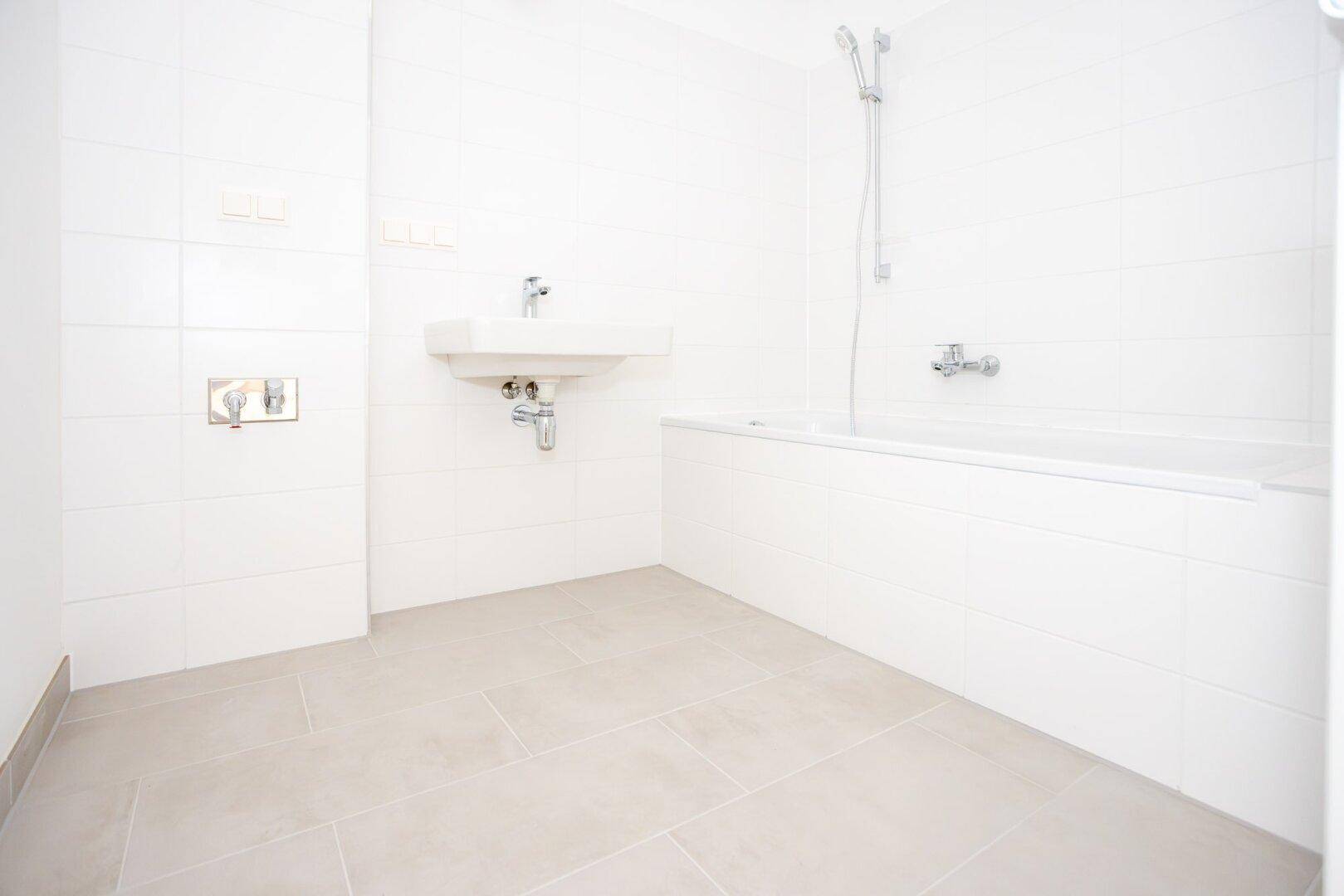 Modernes Badezimmer mit weißen Fliesen, Badewanne und Waschbecken in minimalistischem Design.