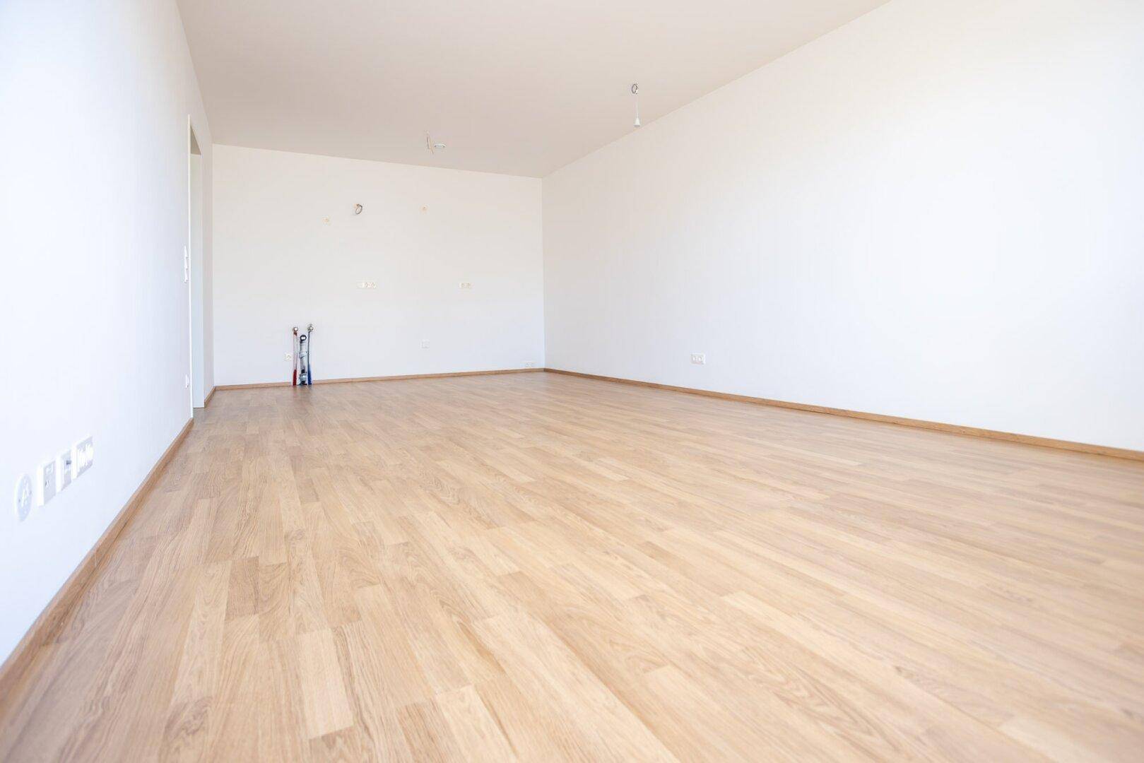 Leerer, heller Raum mit Laminatboden und weißen Wänden, bereit für die individuelle Gestaltung.