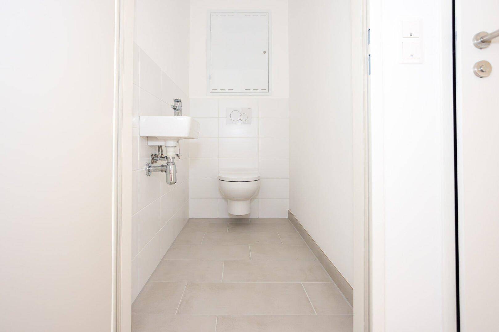 Separates Gäste-WC mit wandhängender Toilette und kleinem Handwaschbecken.