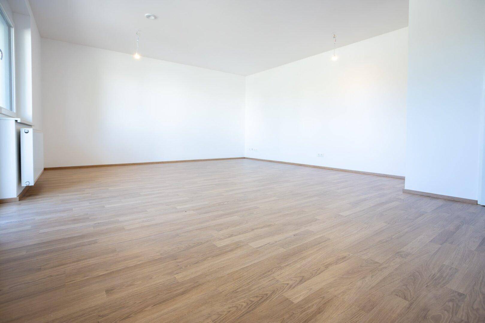 Weitläufiges, unmöbliertes Zimmer mit Laminatboden und großen Fenstern für viel Tageslicht.