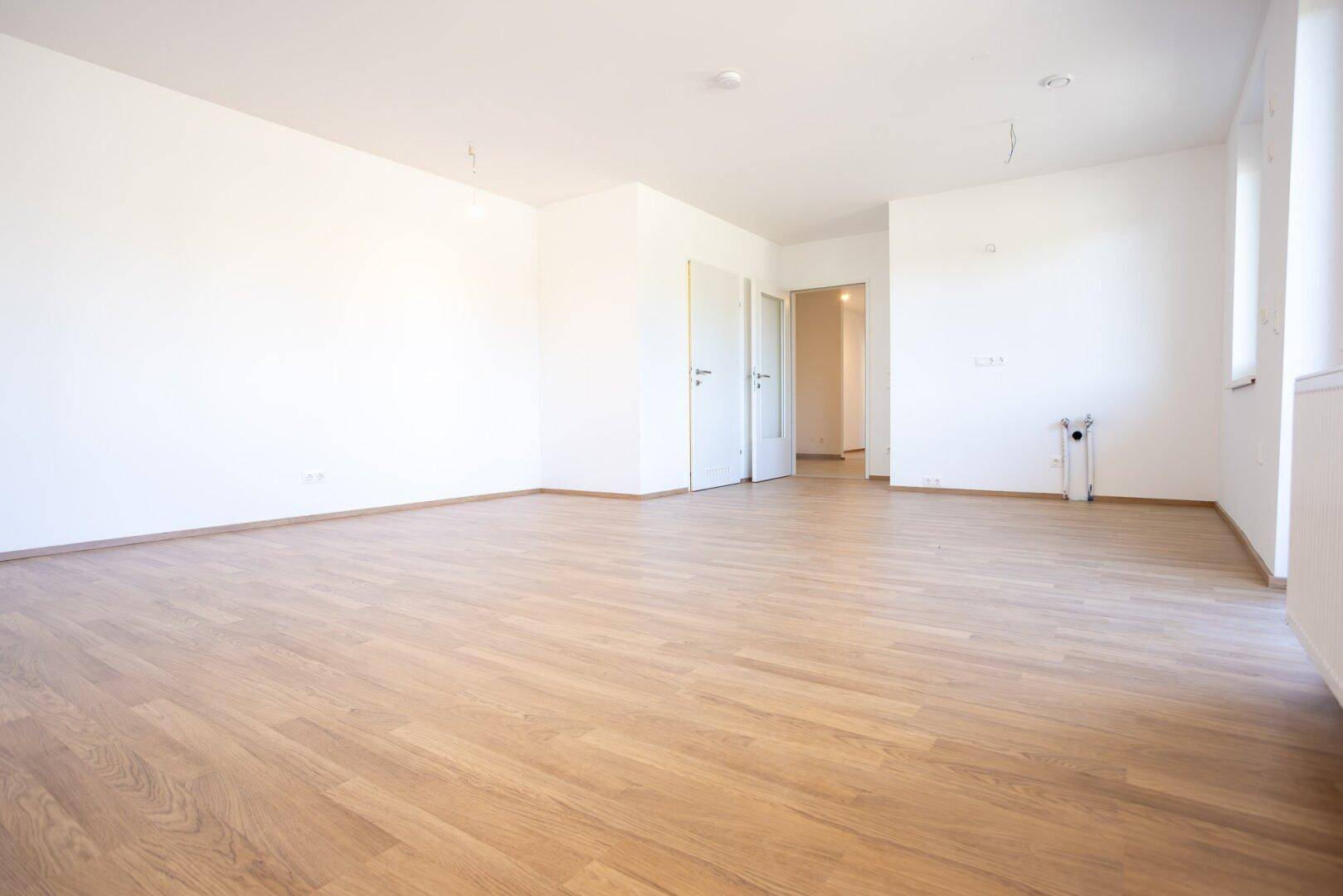 Leeres Zimmer mit Laminatboden, weißen Wänden und Türen, die zu anderen Bereichen führen.
