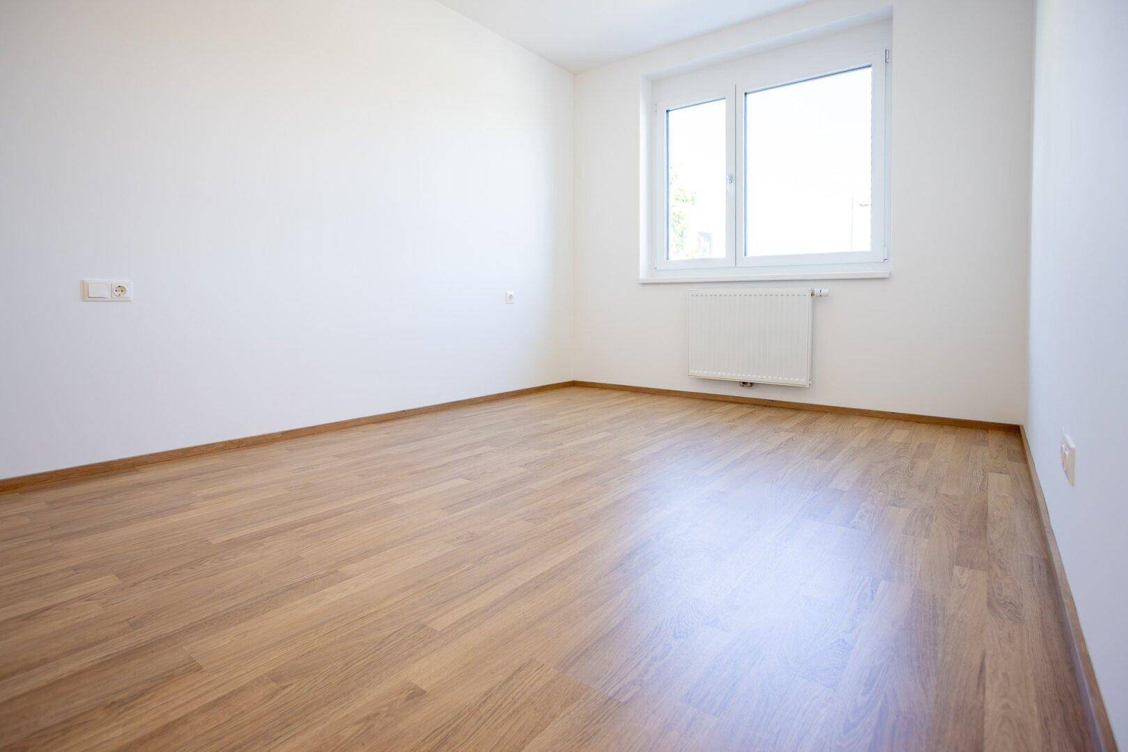 Unmöbliertes Zimmer mit Laminatboden und weißen Wänden, bereit für individuelle Gestaltung.
