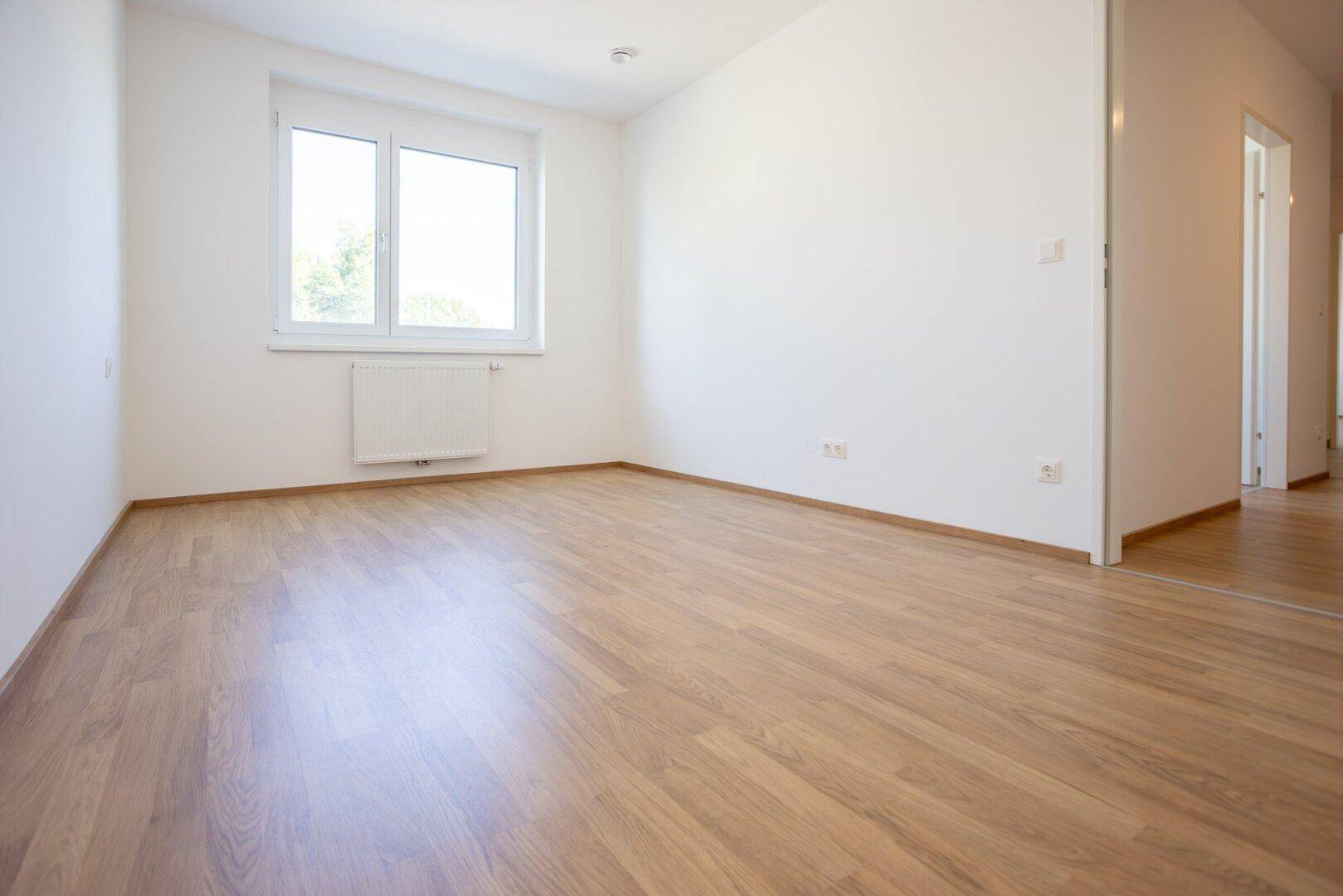 Lichtdurchflutetes Zimmer mit Laminatboden und Zugang zu einem Flur, ideal als Kinderzimmer.