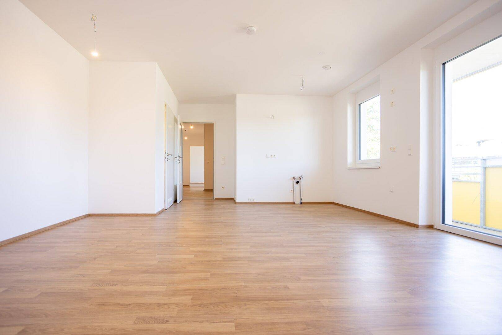 Geräumiges, helles Zimmer mit Laminatboden, weißen Wänden und Zugang zu weiteren Räumen.