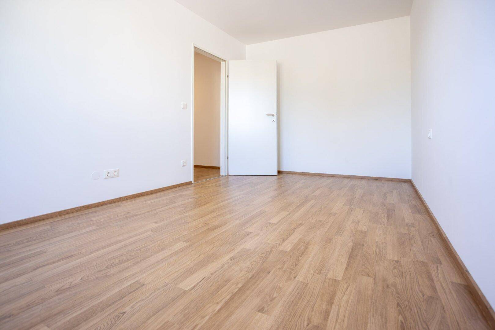 Leeres Zimmer mit Laminatboden und offener Tür, bietet vielseitige Nutzungsmöglichkeiten.