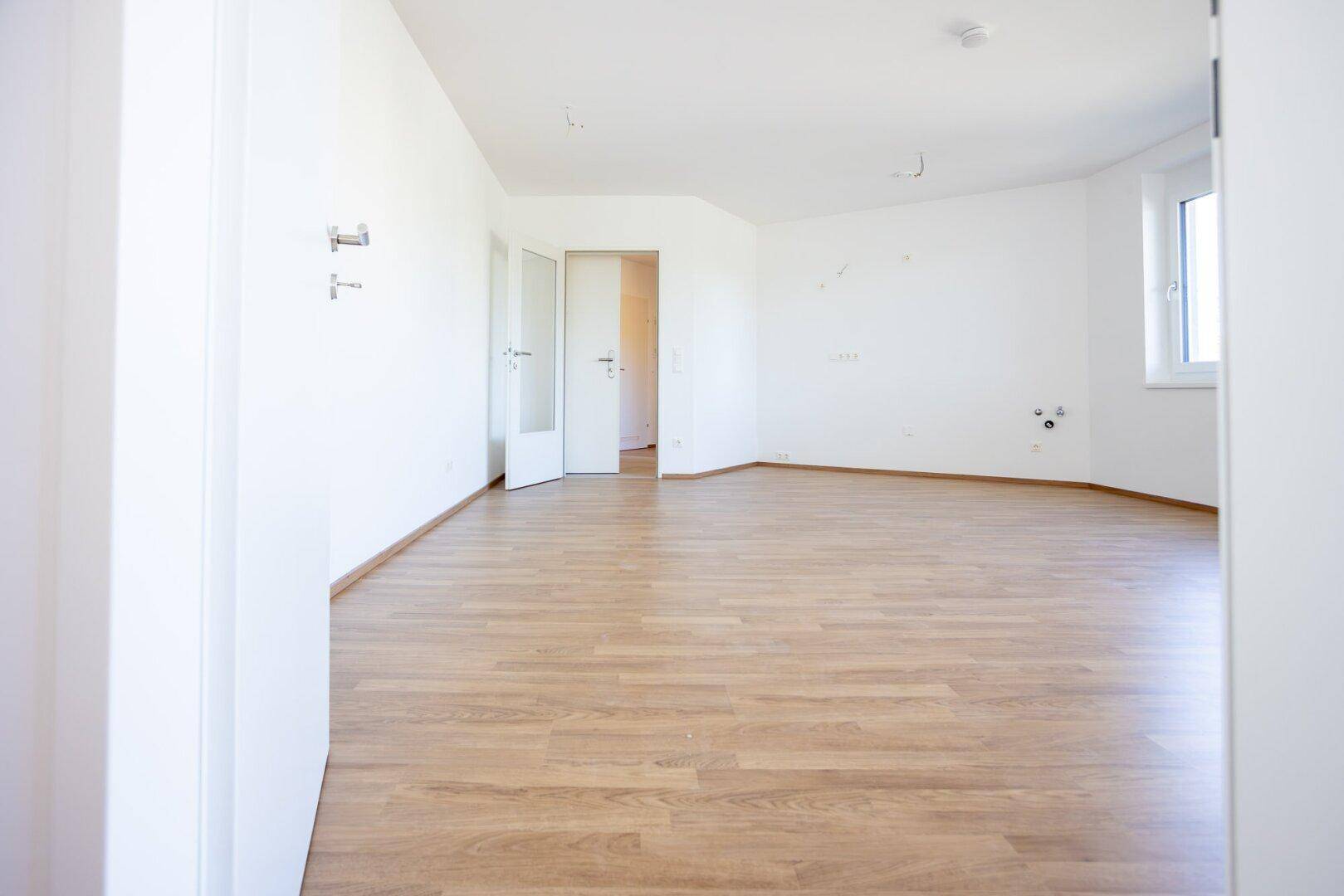 Leerer Küchenbereich mit Laminatboden und Anschlüssen für eine Einbauküche.