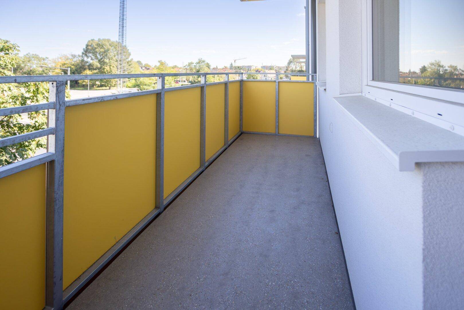 Langer Balkon mit gelben Brüstungselementen und Betonboden.