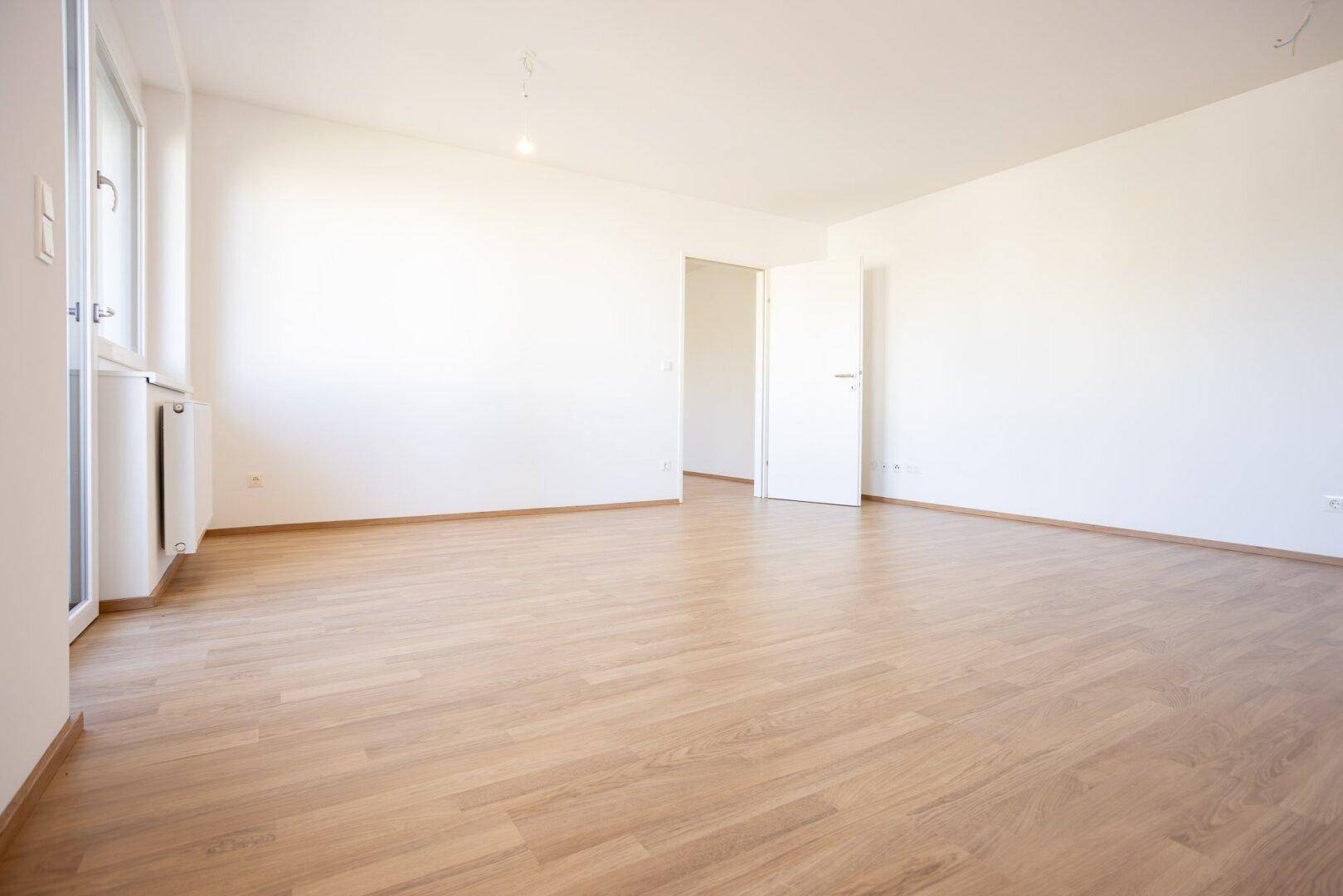 Heller, leerer Wohnraum mit Laminatboden und weiß gestrichenen Wänden.