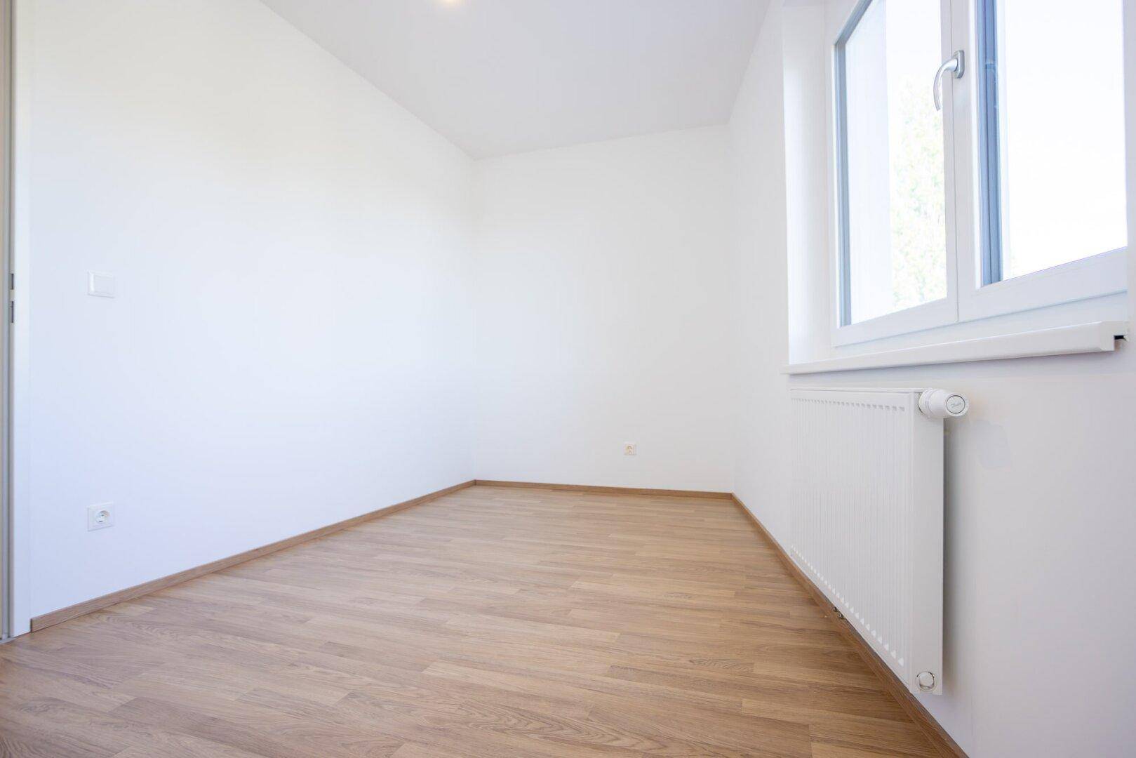 Leeres Zimmer mit Laminatboden, weiß gestrichenen Wänden und Fenster.