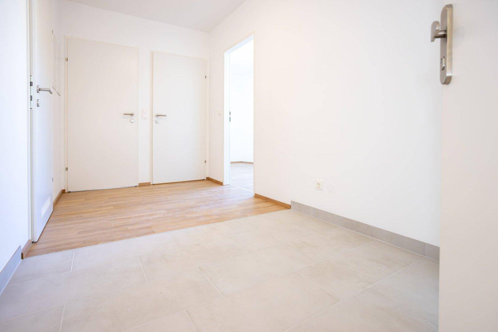 Heller Flur mit Fliesenboden und Übergang zu einem Zimmer mit Laminat.