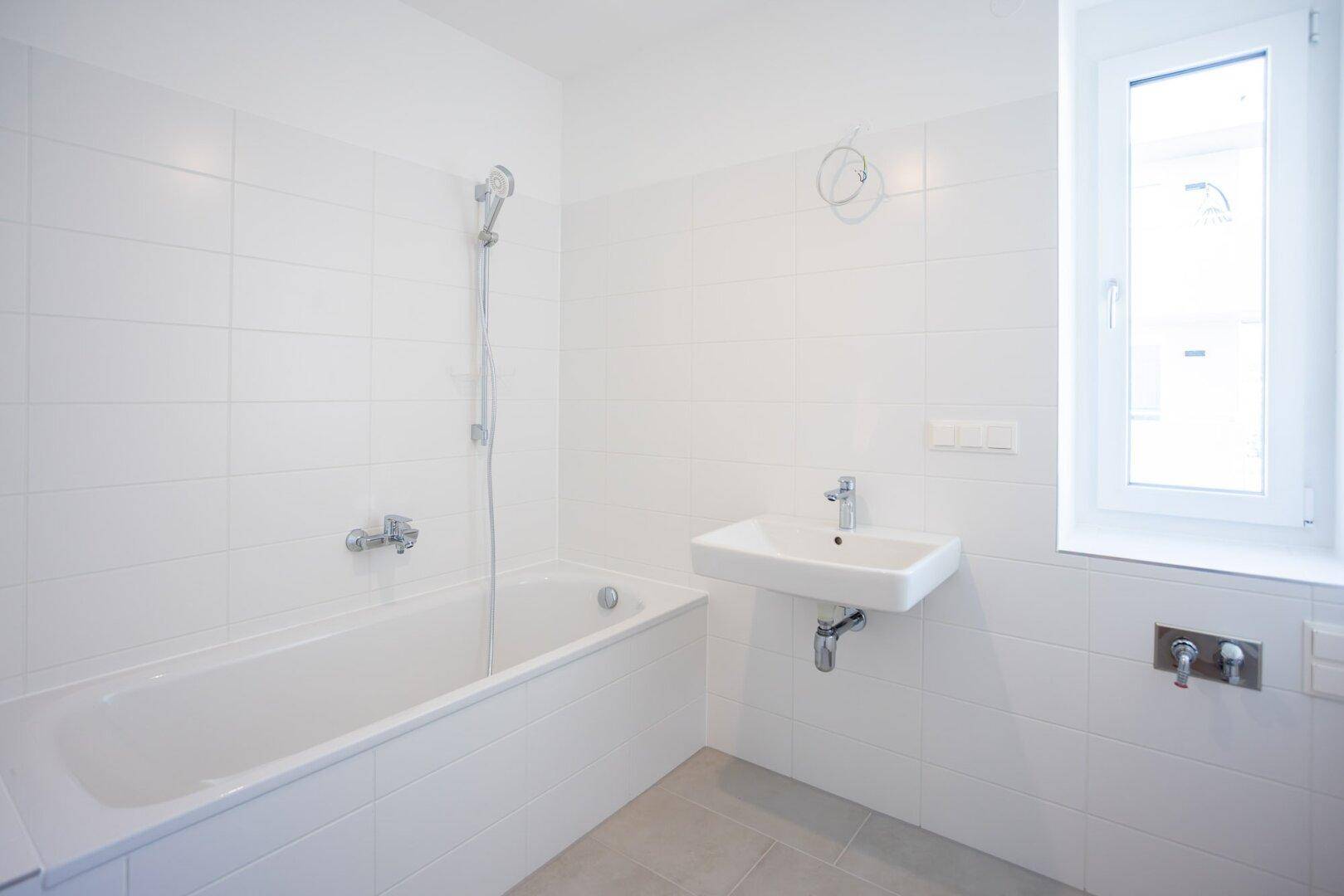 Modernes Badezimmer mit weißen Fliesen, Badewanne und Waschbecken.