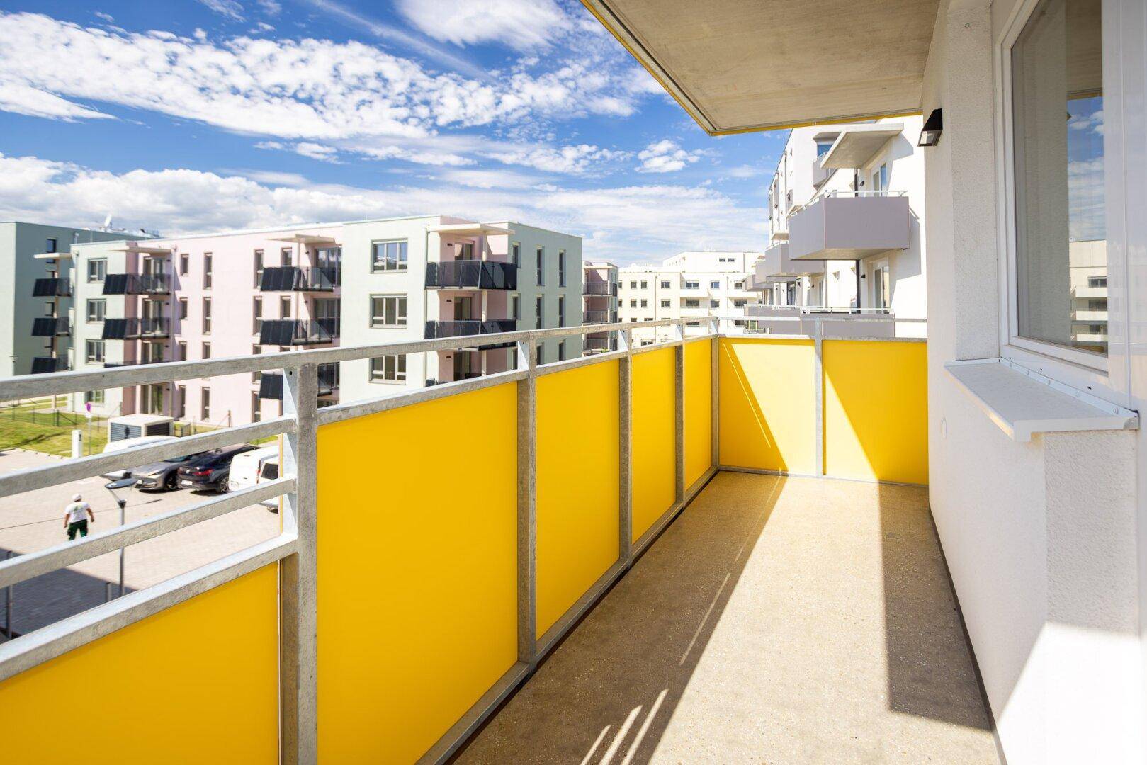 Heller Balkon mit gelben Sichtschutzelementen und Blick auf moderne Wohngebäude.