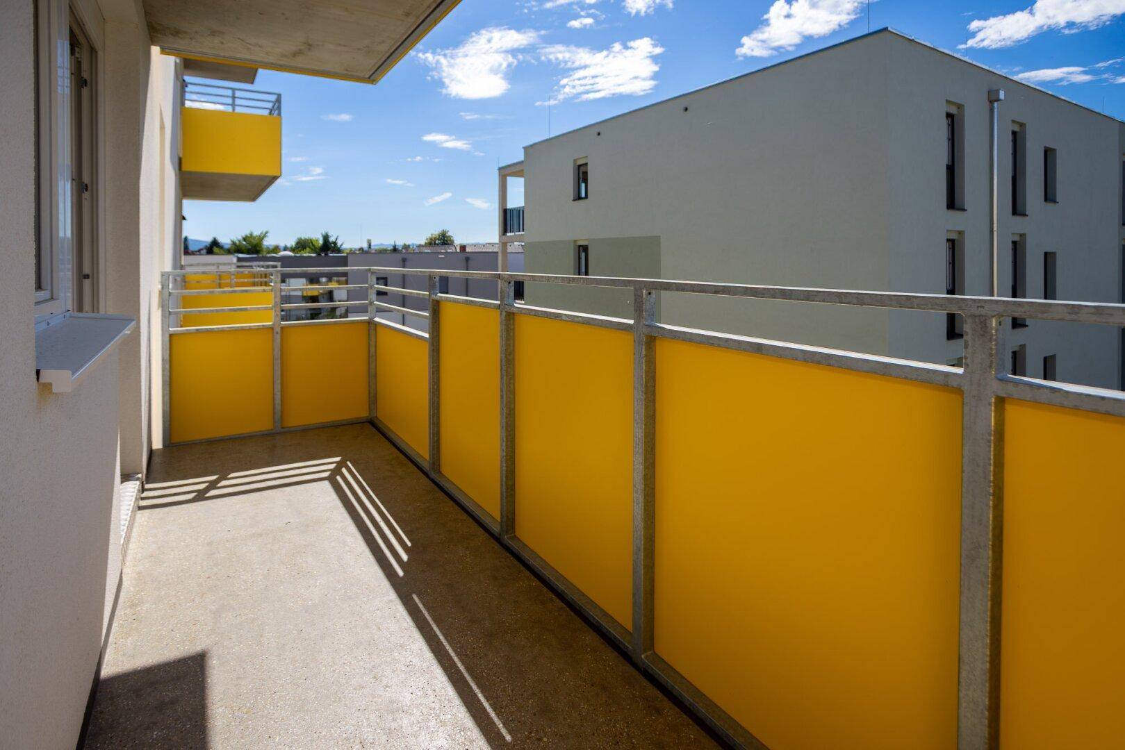 Sonniger Balkon mit gelben Sichtschutzelementen und Blick auf die umliegenden Gebäude.