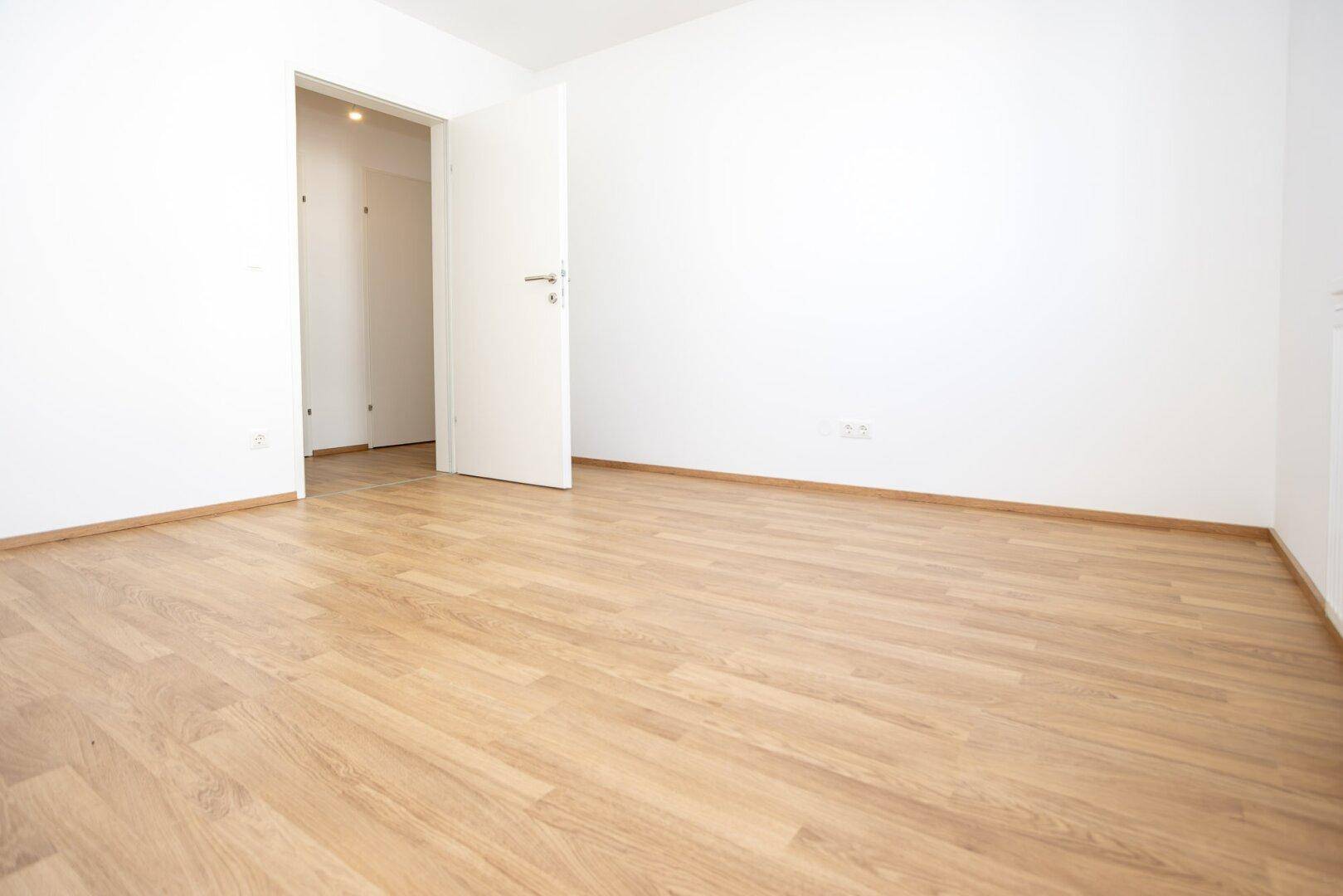 Leeres Zimmer mit hellem Laminatboden und weißen Wänden, bereit zur individuellen Gestaltung.