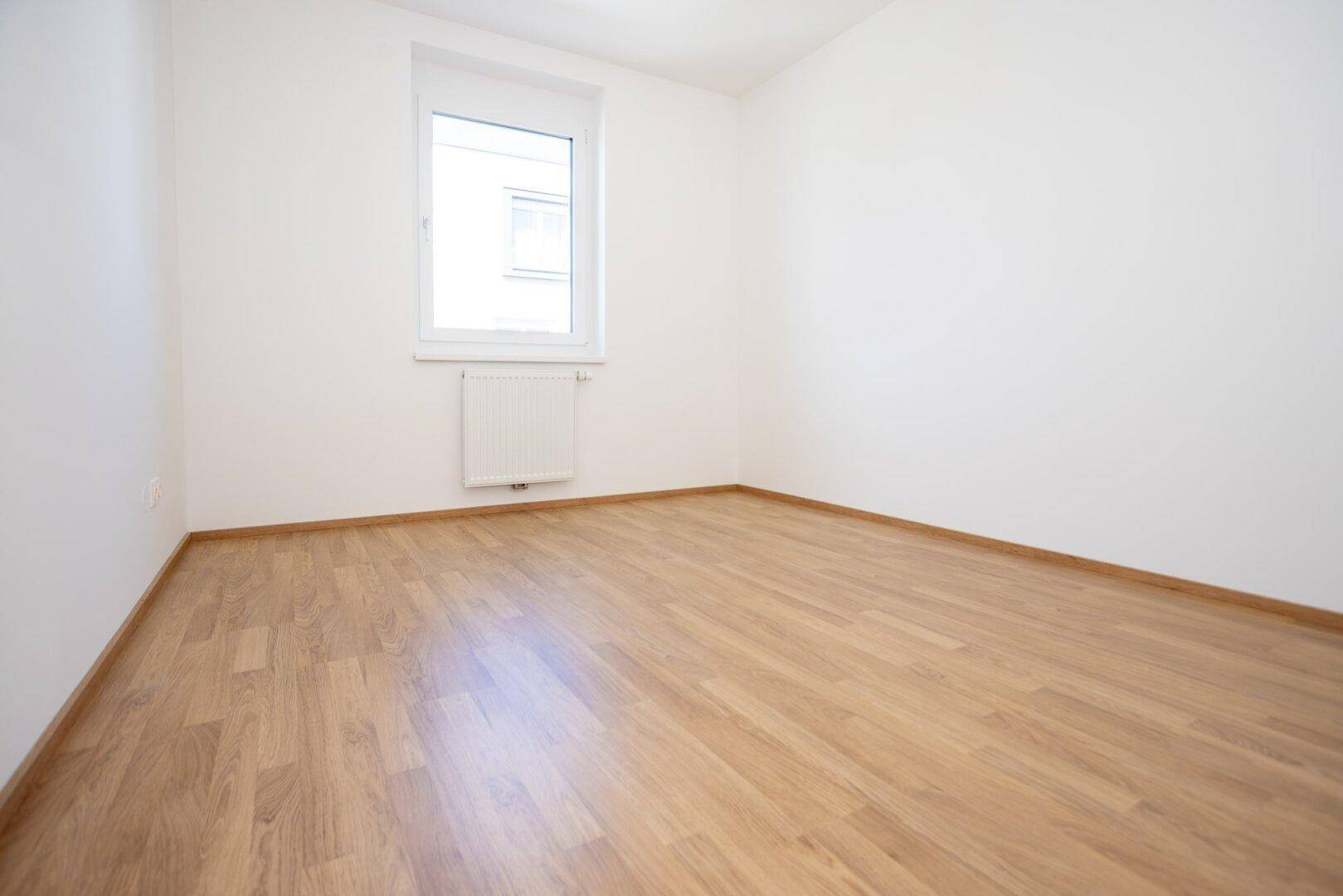 Freundliches Zimmer mit Laminatboden, weißen Wänden und einem Fenster für viel Tageslicht.