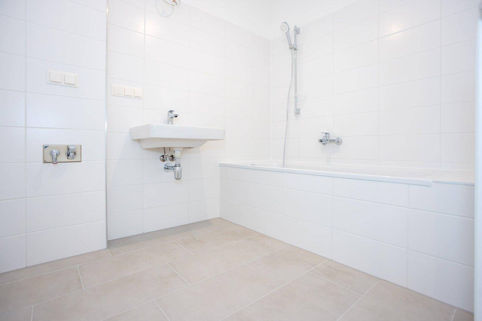 Modernes Badezimmer mit weißen Fliesen, Waschbecken und einer Badewanne mit Duschfunktion.