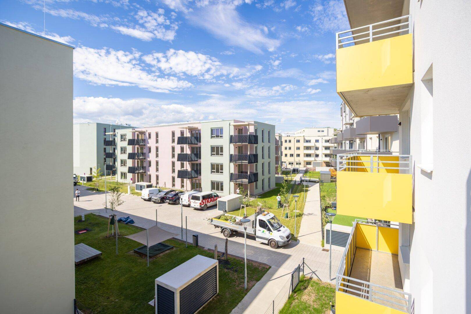 Moderne Wohnanlage mit mehreren Gebäuden, Grünflächen und Parkplätzen unter blauem Himmel.
