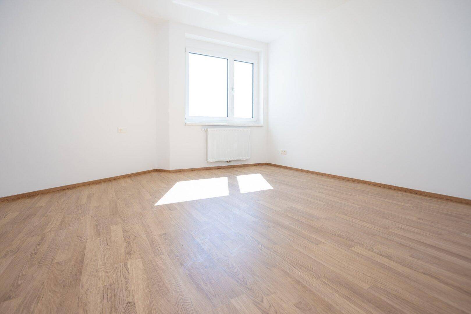 Helles Schlafzimmer mit Laminatboden, weißen Wänden und einem Fenster für viel Tageslicht.