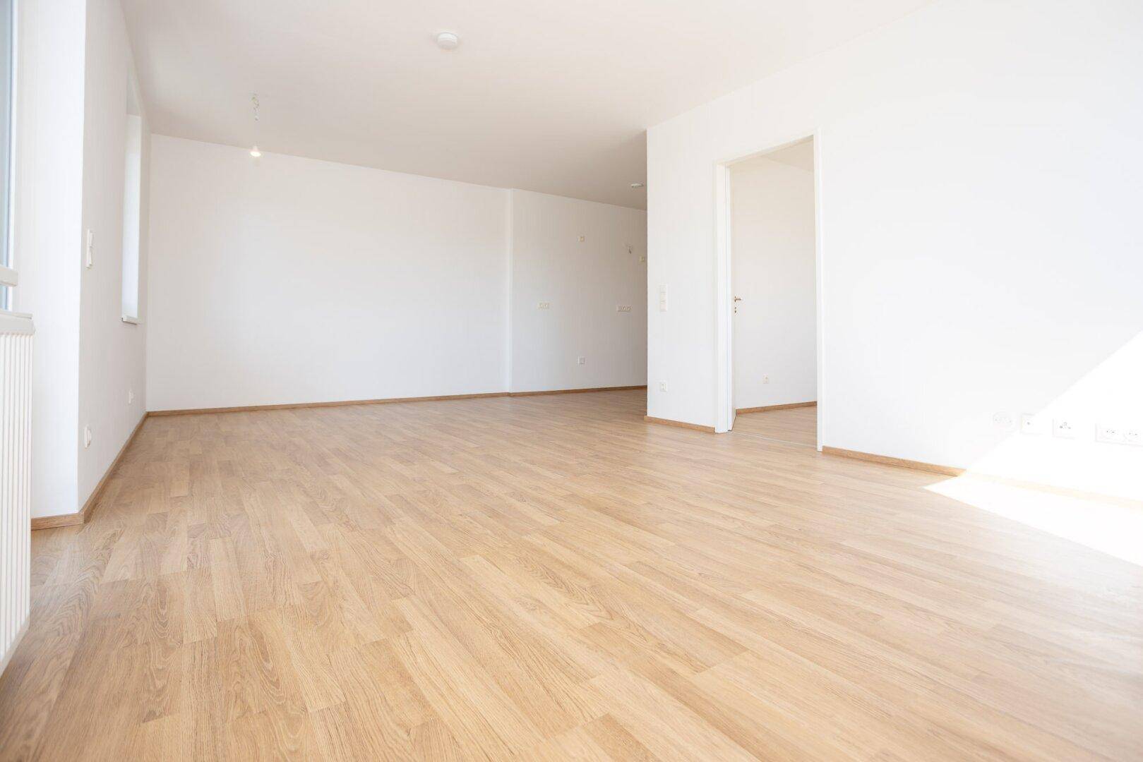 Geräumiger, heller Raum mit Laminatboden und weißen Wänden, bereit für individuelle Gestaltung.