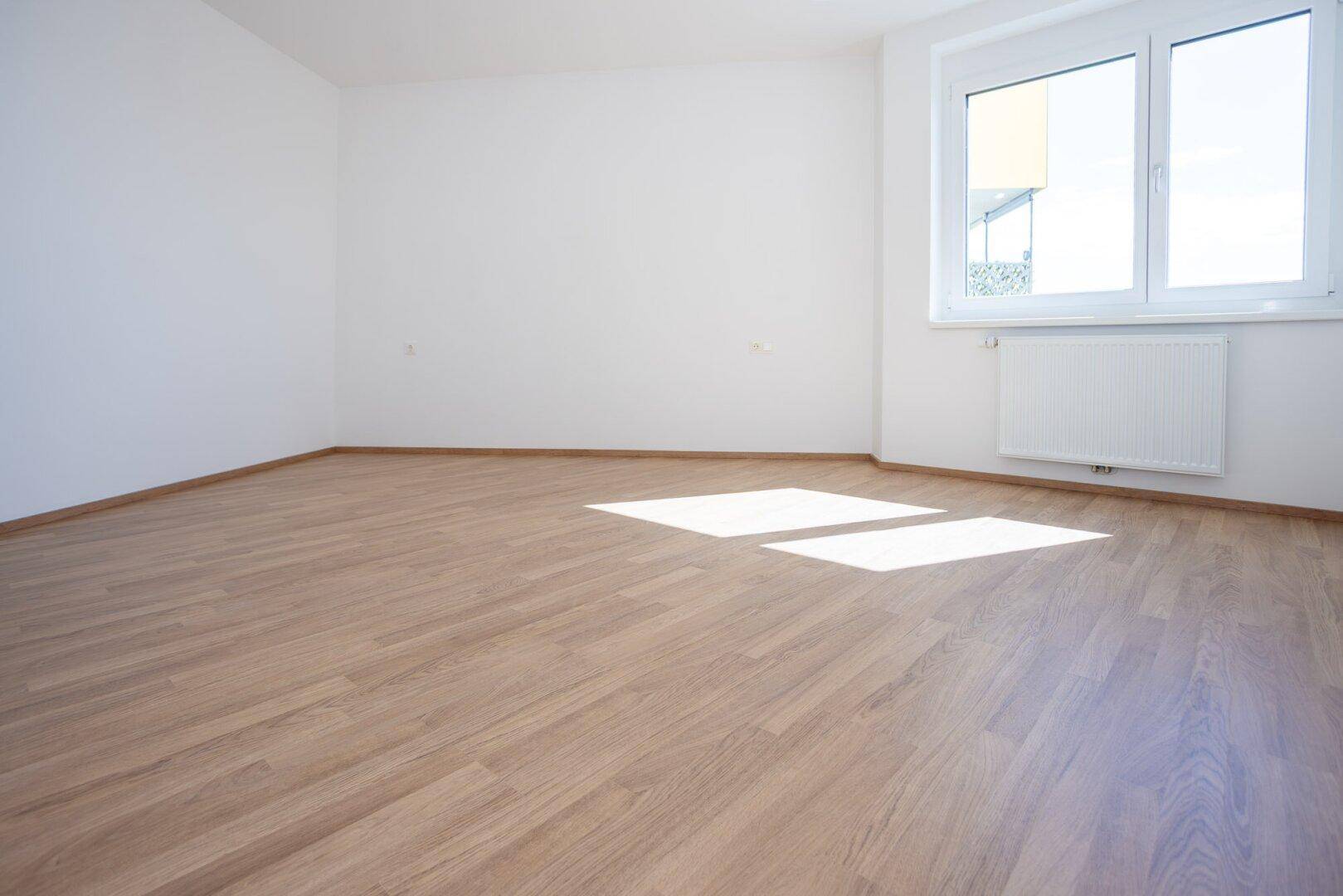 Geräumiges Schlafzimmer mit hellem Laminatboden, weißen Wänden und einem großen Fenster.