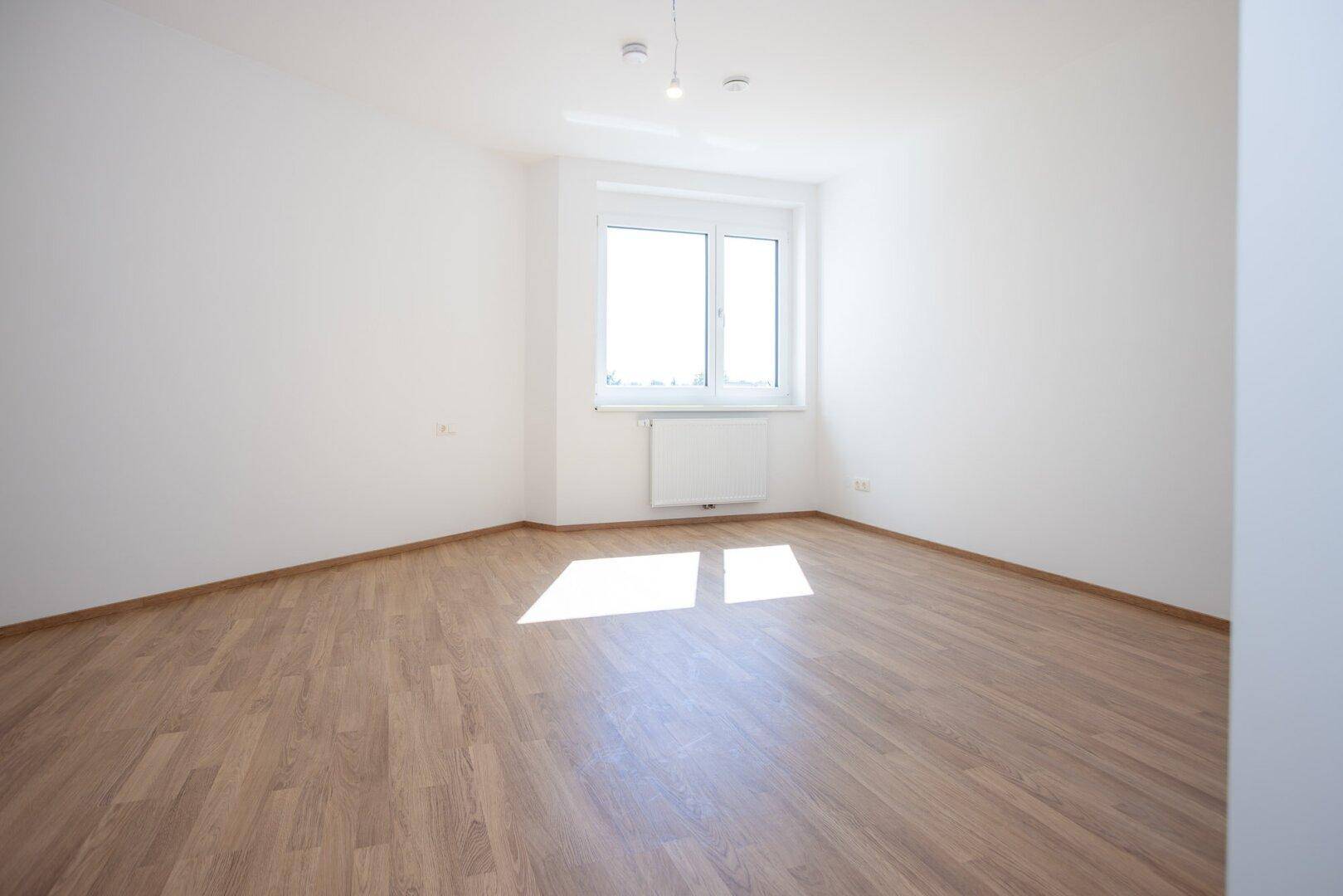Freundliches Schlafzimmer mit Laminatboden, weißen Wänden und einem Fenster, das viel Licht hereinlässt.