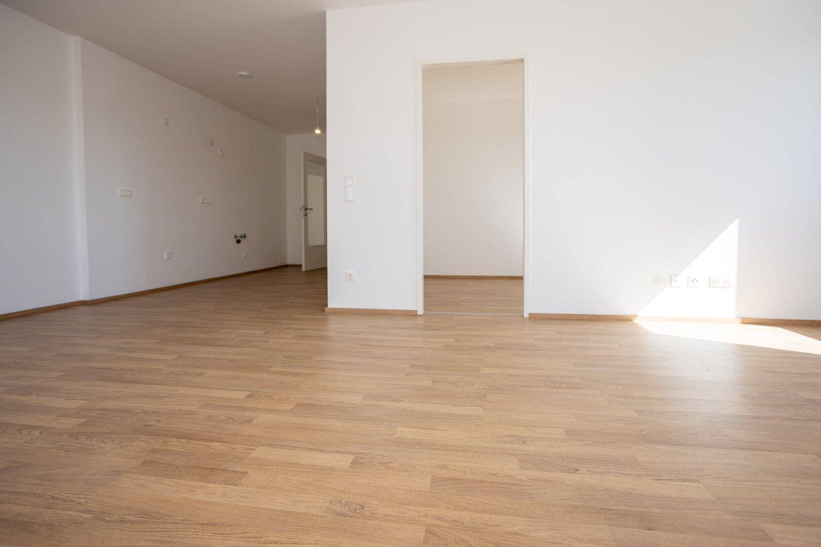 Heller, leerer Raum mit Laminatboden und weißen Wänden, ideal für ein offenes Wohnkonzept.