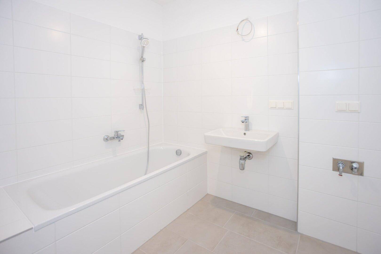 Modernes Badezimmer mit weißen Fliesen, Badewanne mit Duschfunktion und einem Waschbecken.