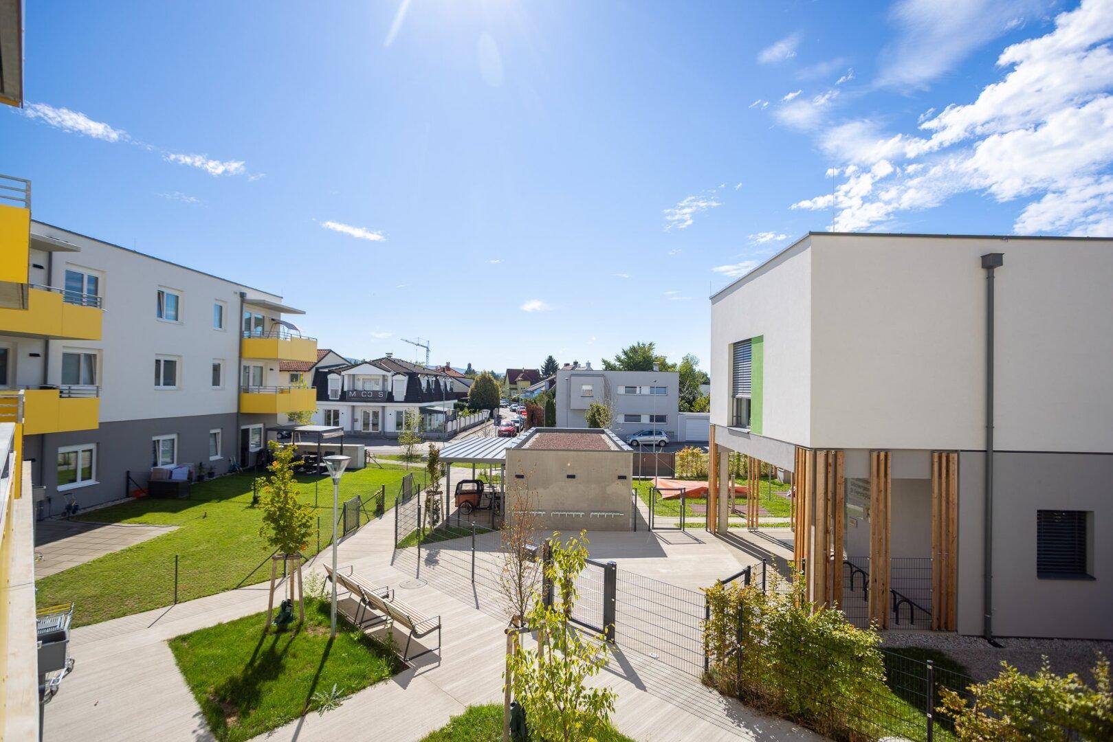 Moderne Wohngebäude mit gepflegten Grünflächen und einem Gemeinschaftsbereich unter blauem Himmel.