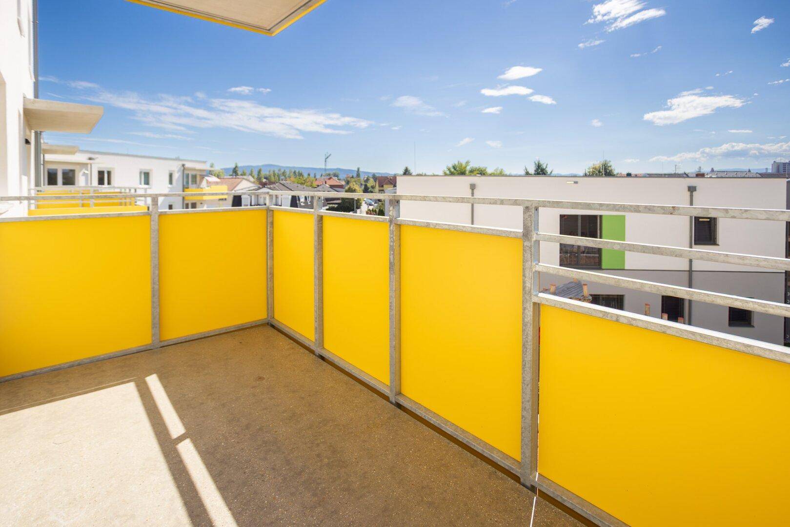 Geräumiger Balkon mit leuchtend gelben Paneelen und weitem Blick über die Wohnanlage.