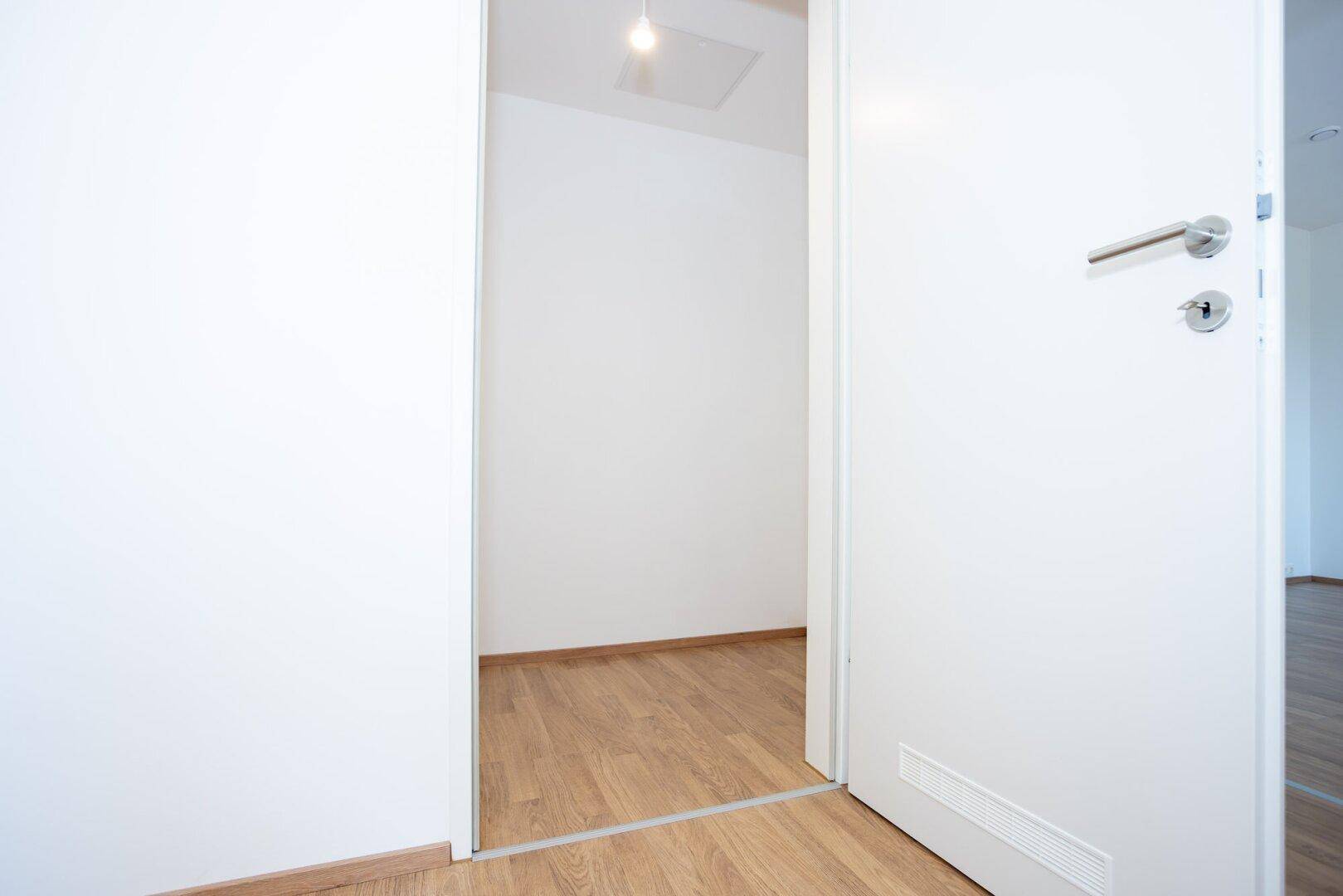 Offene Tür zu einem weiteren hellen Raum mit Laminatboden, der eine Verbindung zwischen den Bereichen schafft.